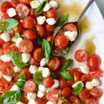 Caprese Salad with Cherry Tomatoes on white oval platter with serving spoon.