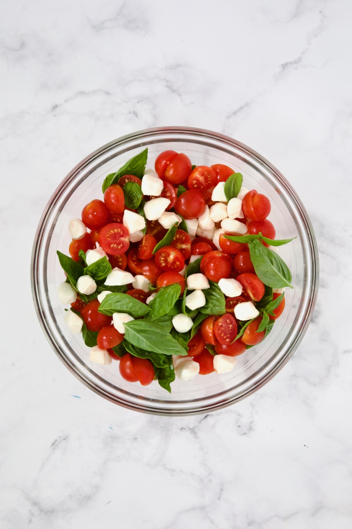 Fresh basil, mozzarella pearls and halved cherry tomatoes in glass bowl mixed together.