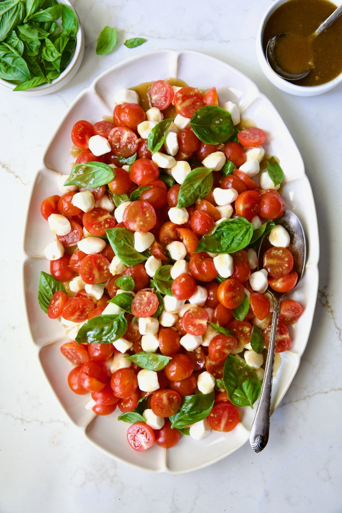 Caprese Salad with Cherry Tomatoes on white oval platter with serving spoon.