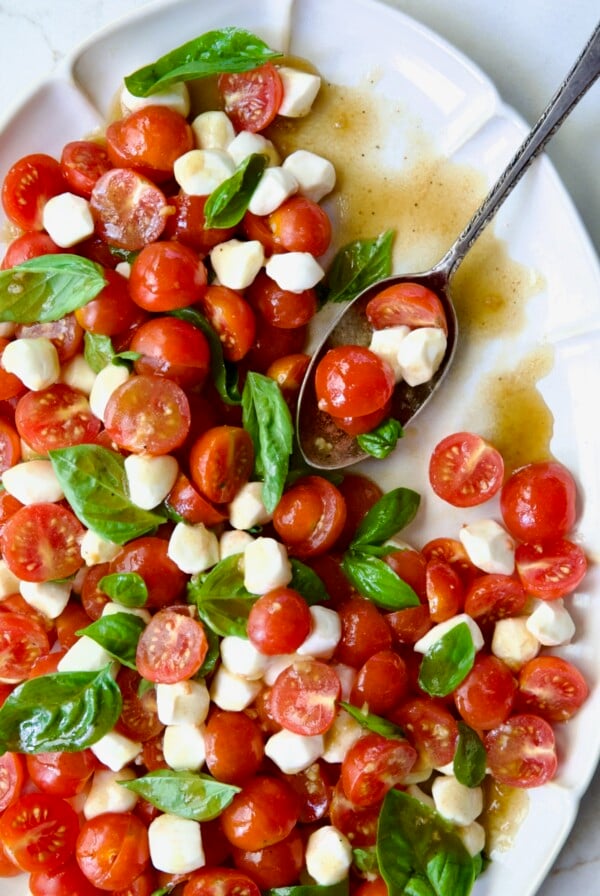 Caprese Salad with Cherry Tomatoes on white oval platter with serving spoon.