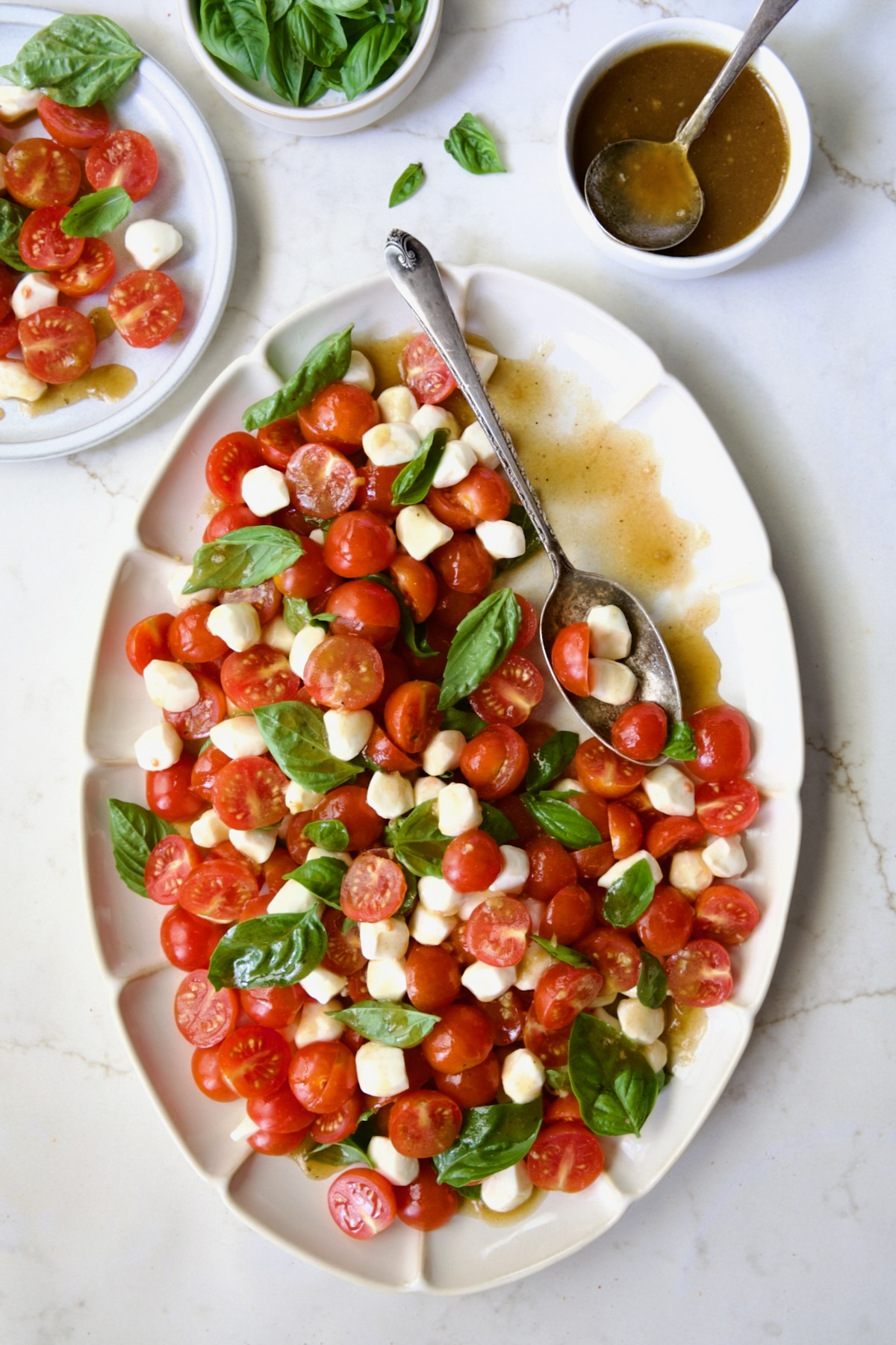Caprese Salad with Cherry Tomatoes on white oval platter with serving spoon.