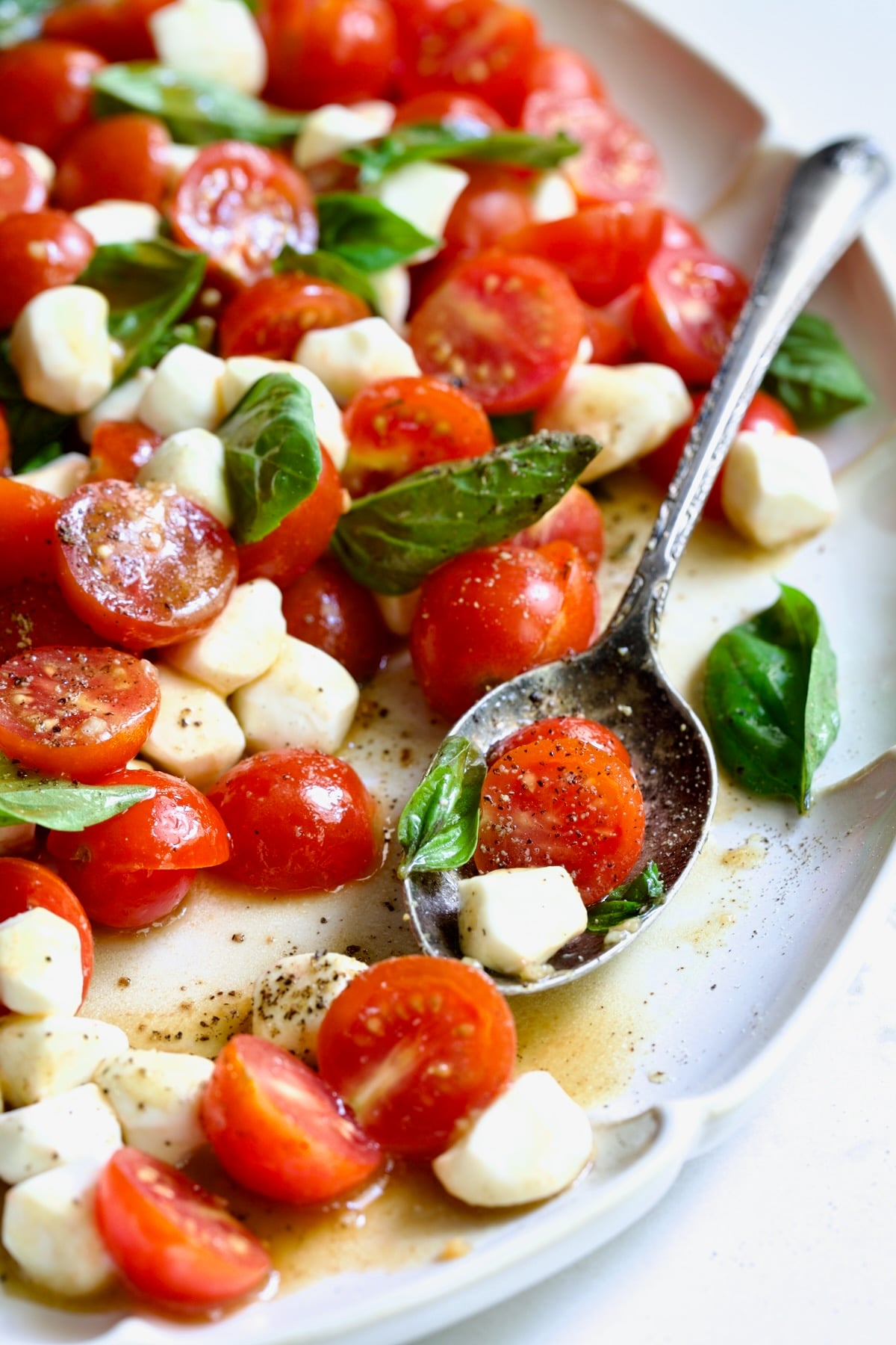 Caprese Salad with Cherry Tomatoes on white oval platter with serving spoon.