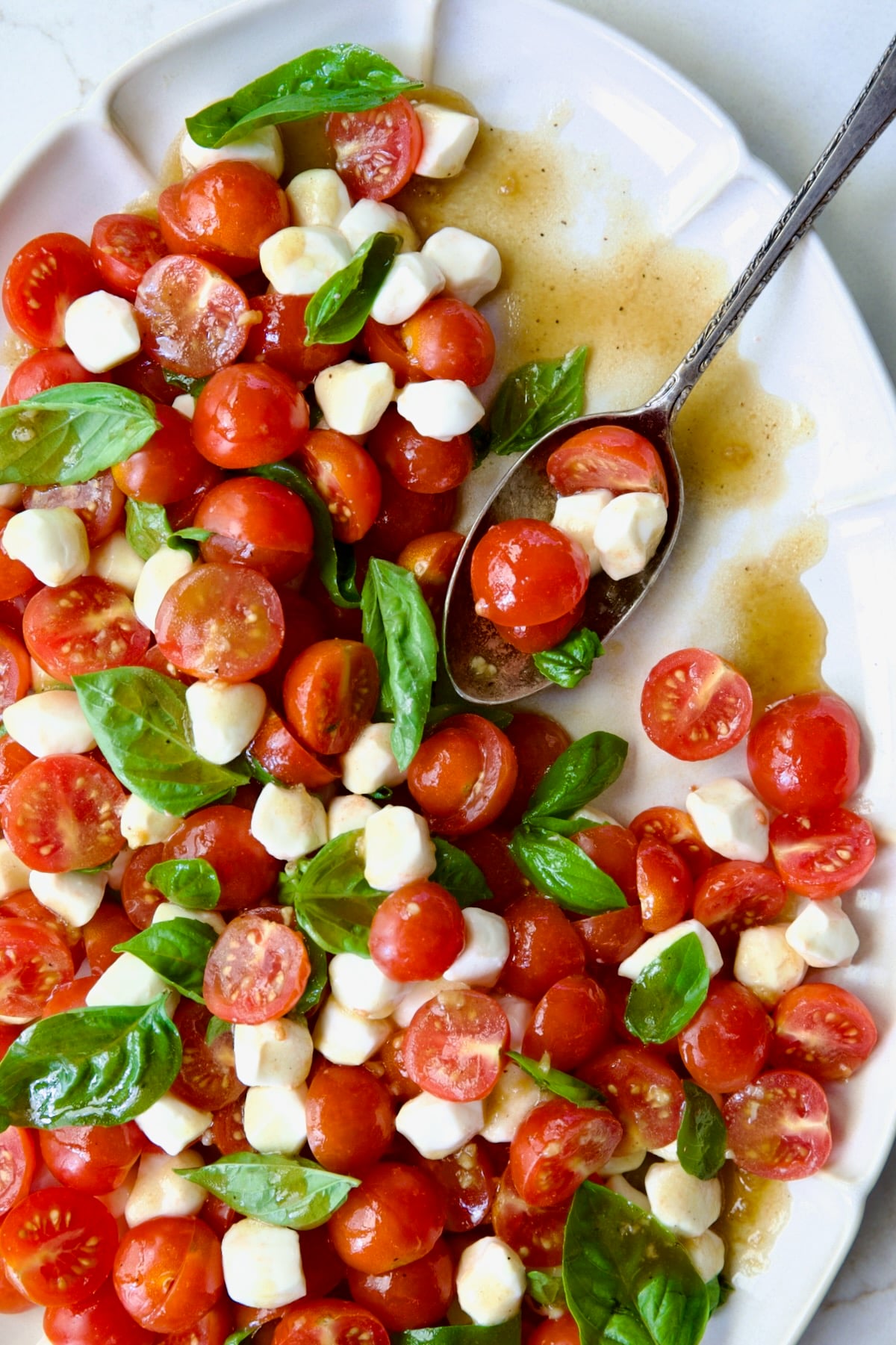 Caprese Salad with Cherry Tomatoes on white oval platter with serving spoon.