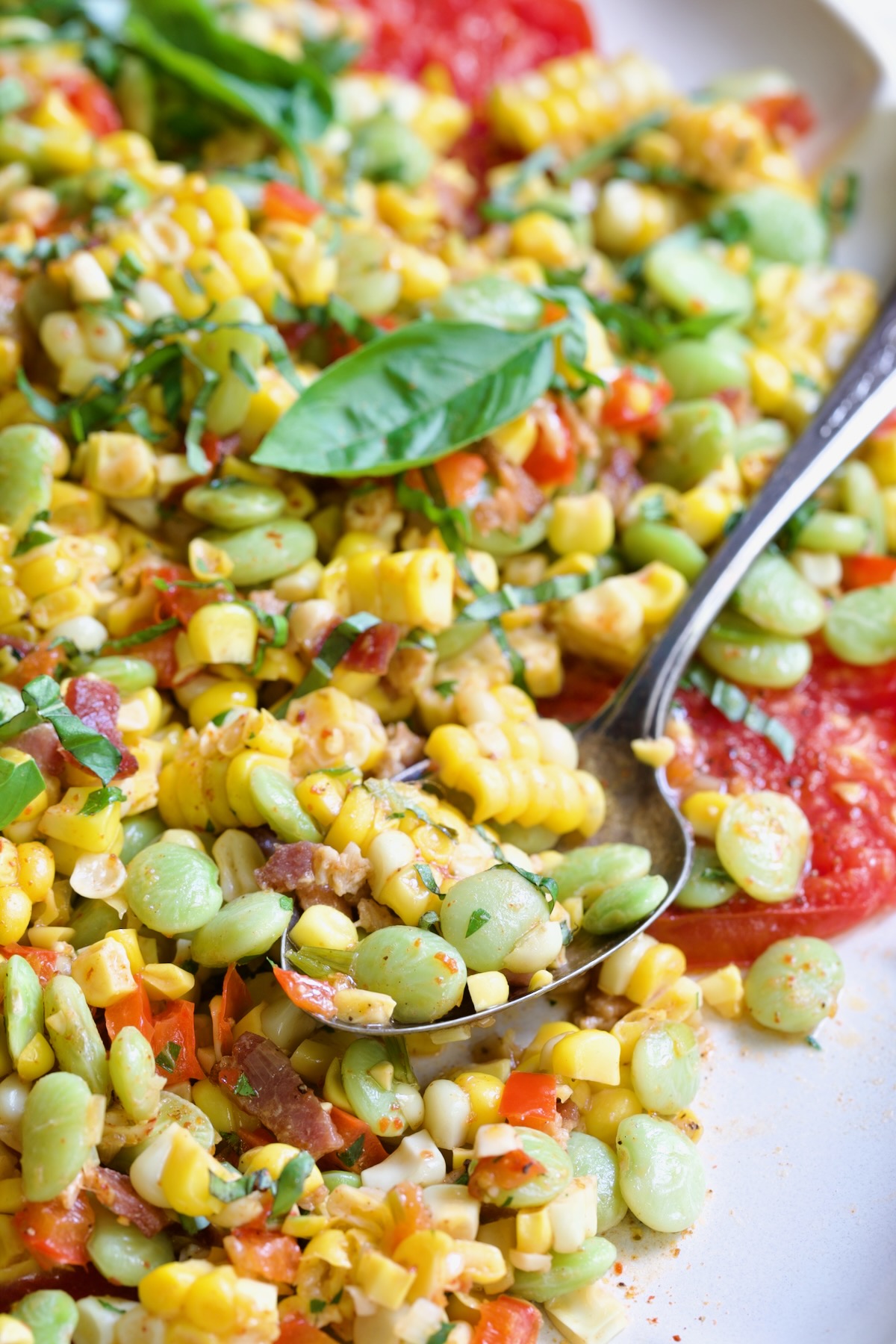 Grilled Corn Succotash garnished with fresh basil on white oval platter with serving spoon scooping some up.