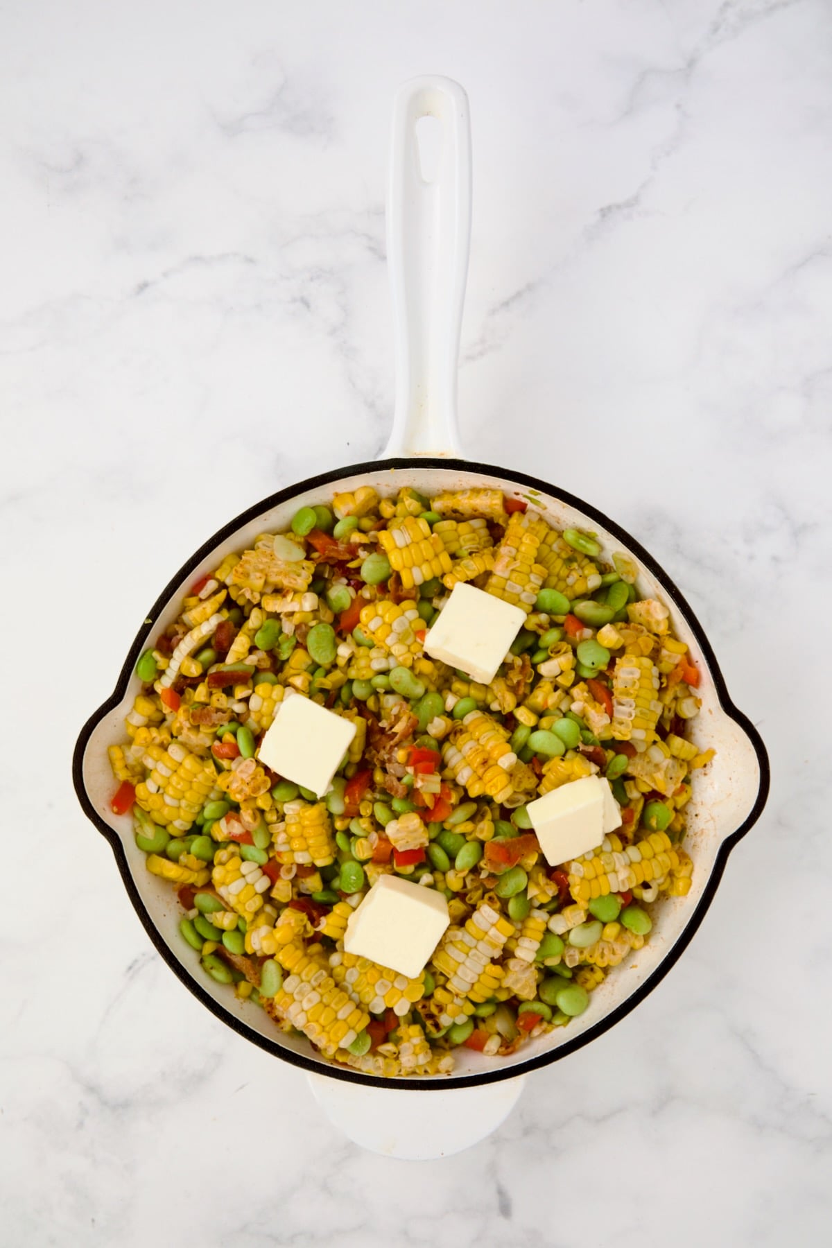 Succotash in white enamel cast iron skillet with four pats of butter on top.