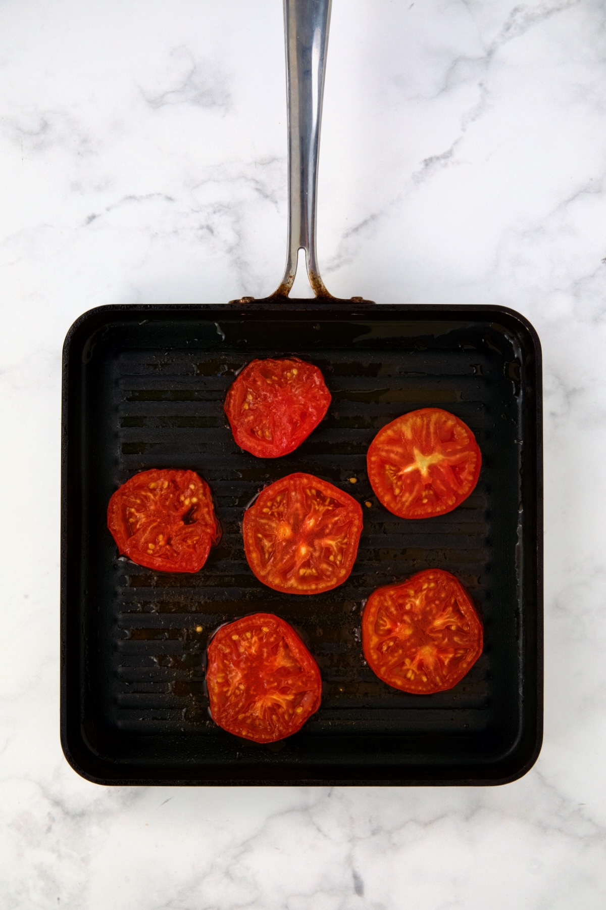 Six tomato slices being grilled on grill pan.