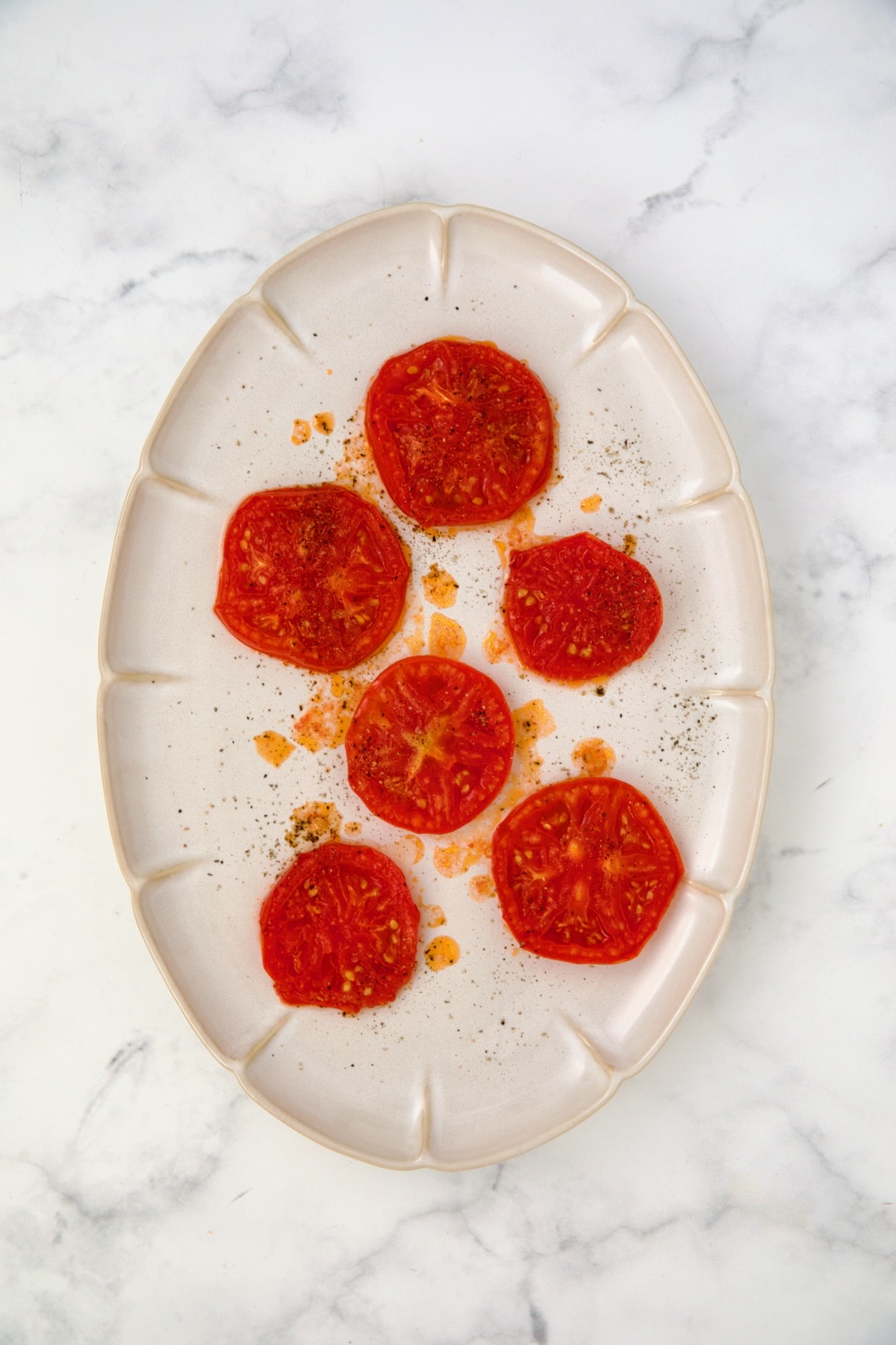 Six grilled tomato slices on white oval platter.