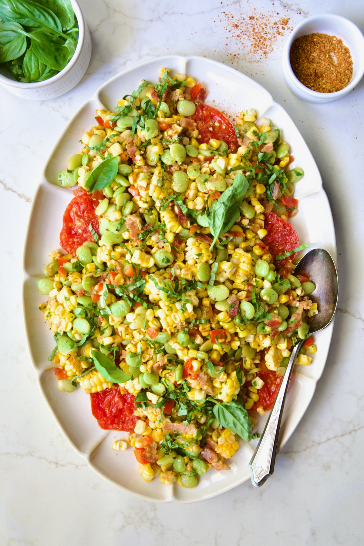 Grilled Corn Succotash on white oval platter garnished with fresh basil leaves.
