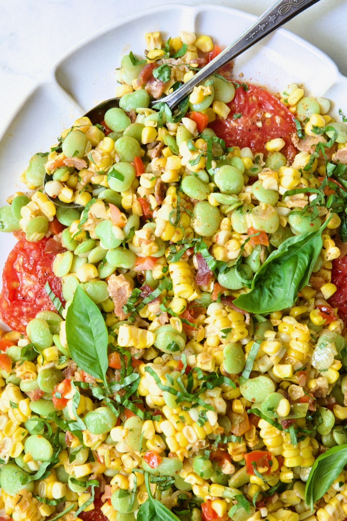Grilled Corn Succotash on white oval platter with serving spoon garnished with fresh basil leaves.