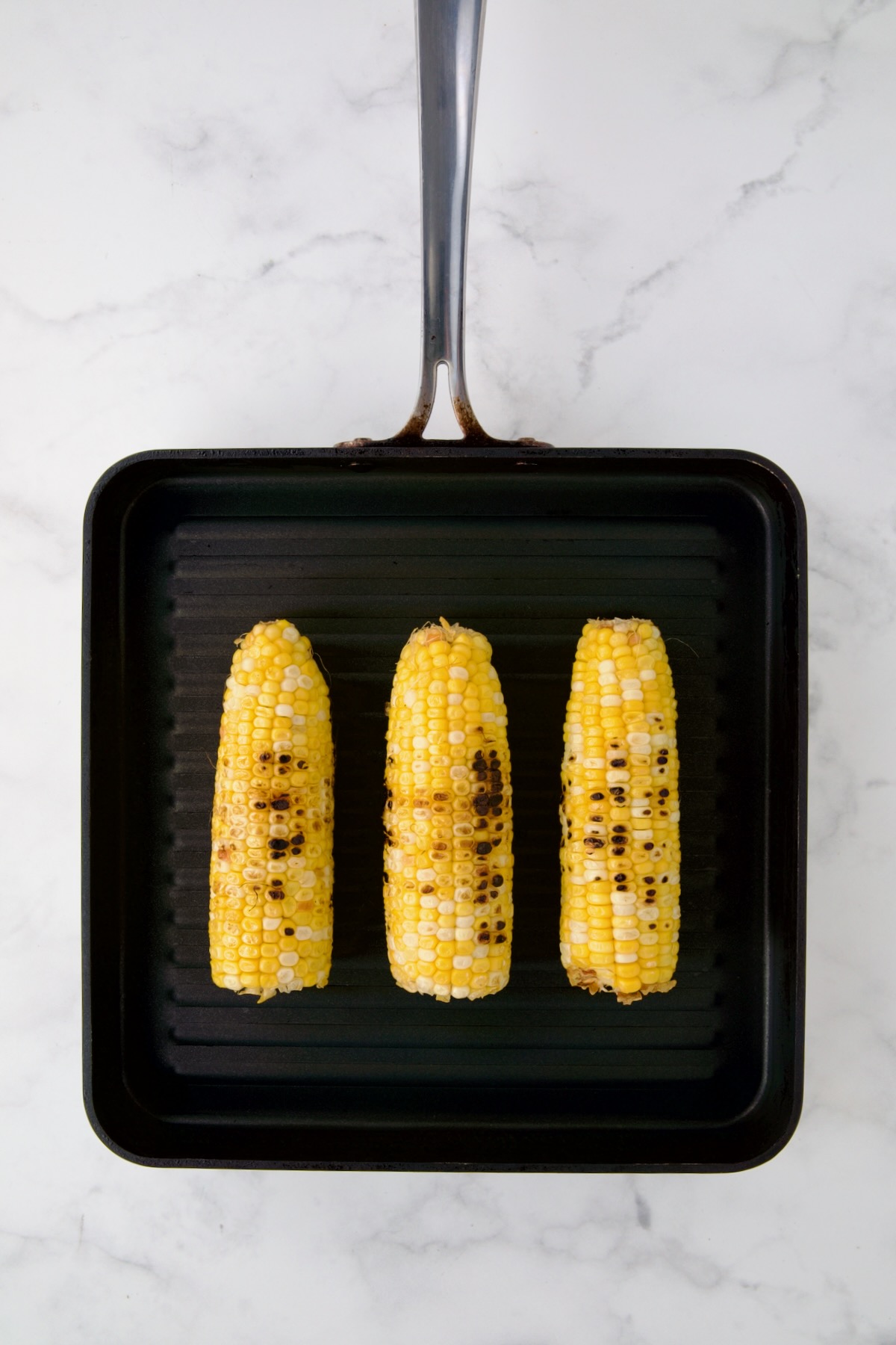 Three ears of corn being grilled on grill pan.