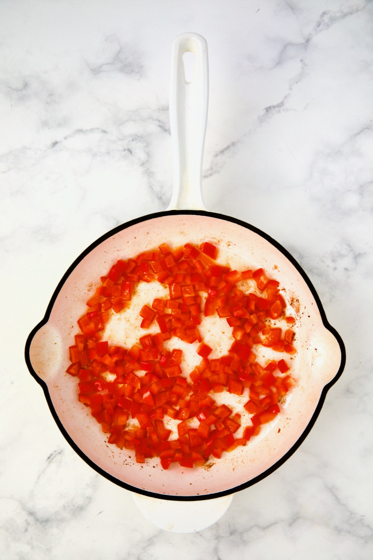 Cooked red bell pepper in white enamel cast iron skillet.