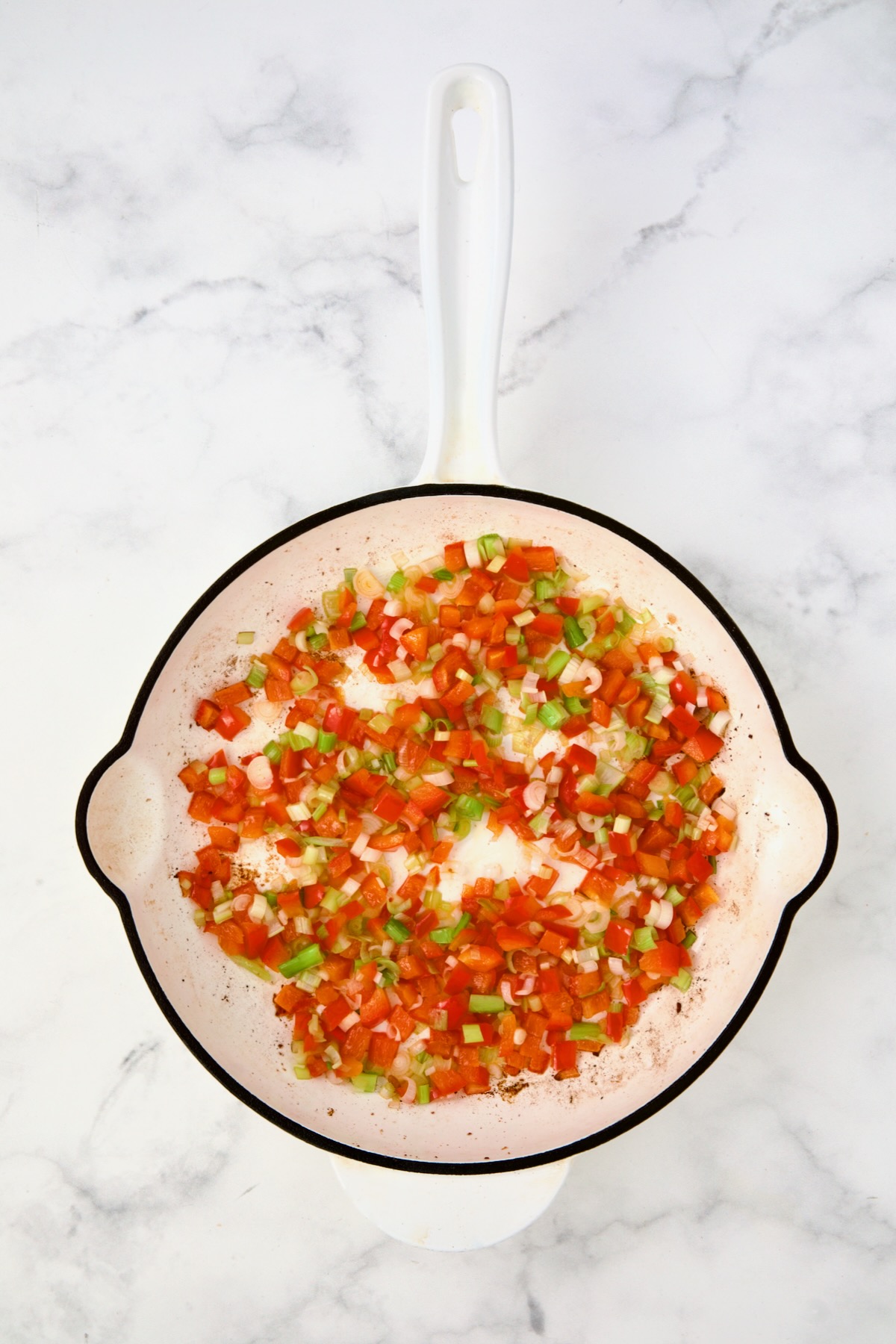 Cooked red bell pepper and scallion in white enamel cast iron skillet.
