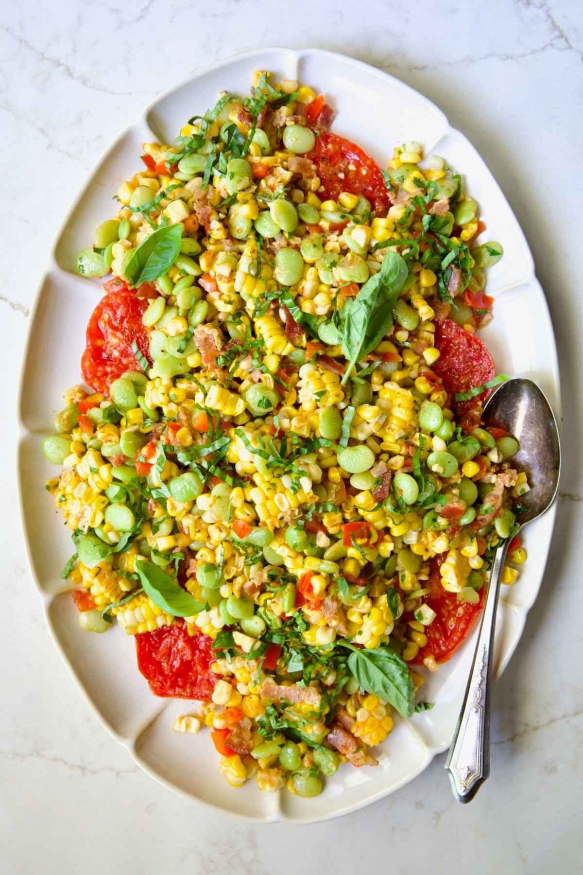 Grilled Corn Succotash on white oval platter garnished with fresh basil leaves.