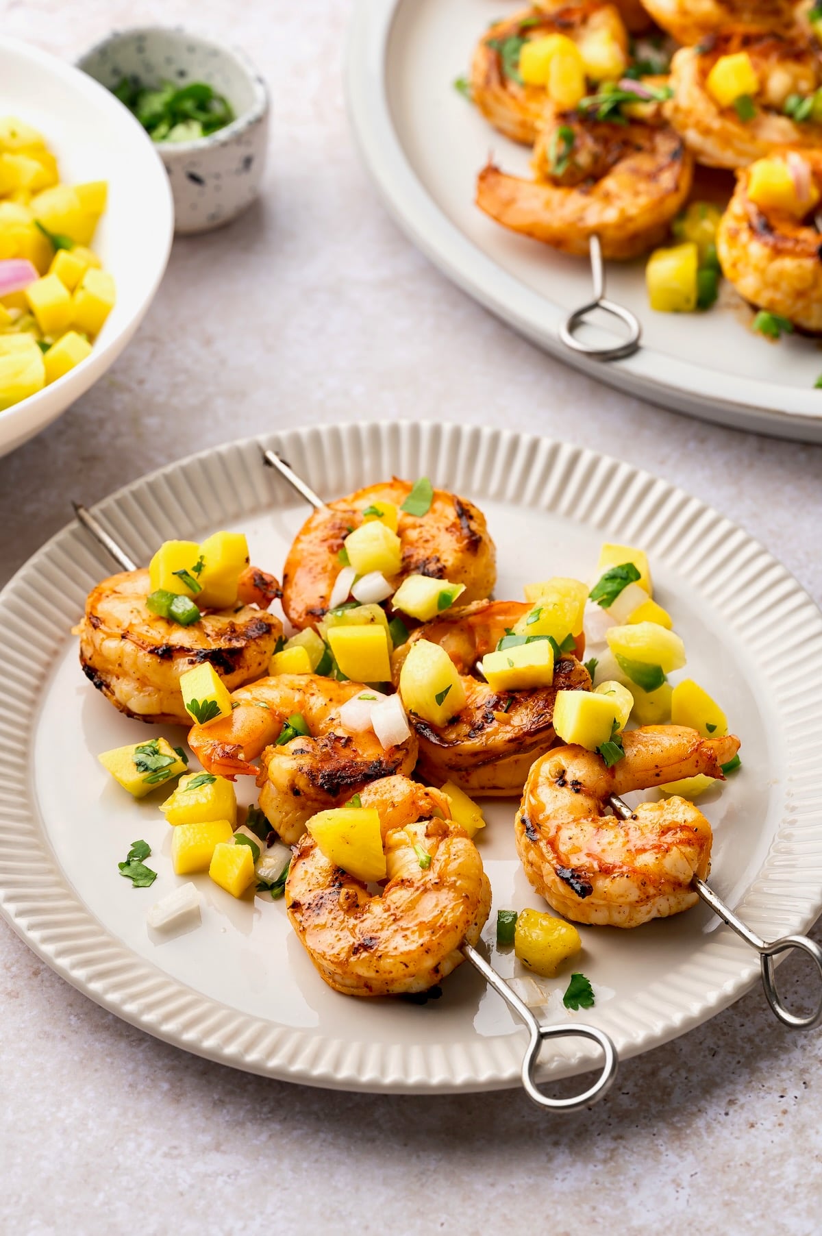 Two Grilled Shrimp Skewers with Mango Pineapple Salsa on small round white plate.