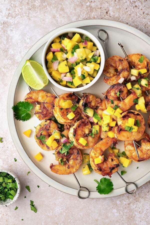Grilled Shrimp Skewers with Mango Pineapple Salsa on round white plate.