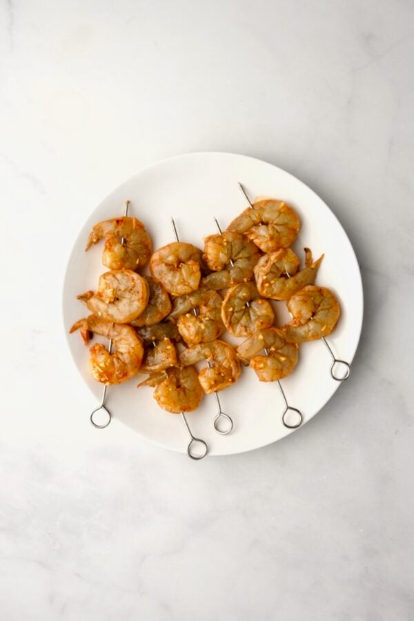 Uncooked shrimp skewers on round white plate.
