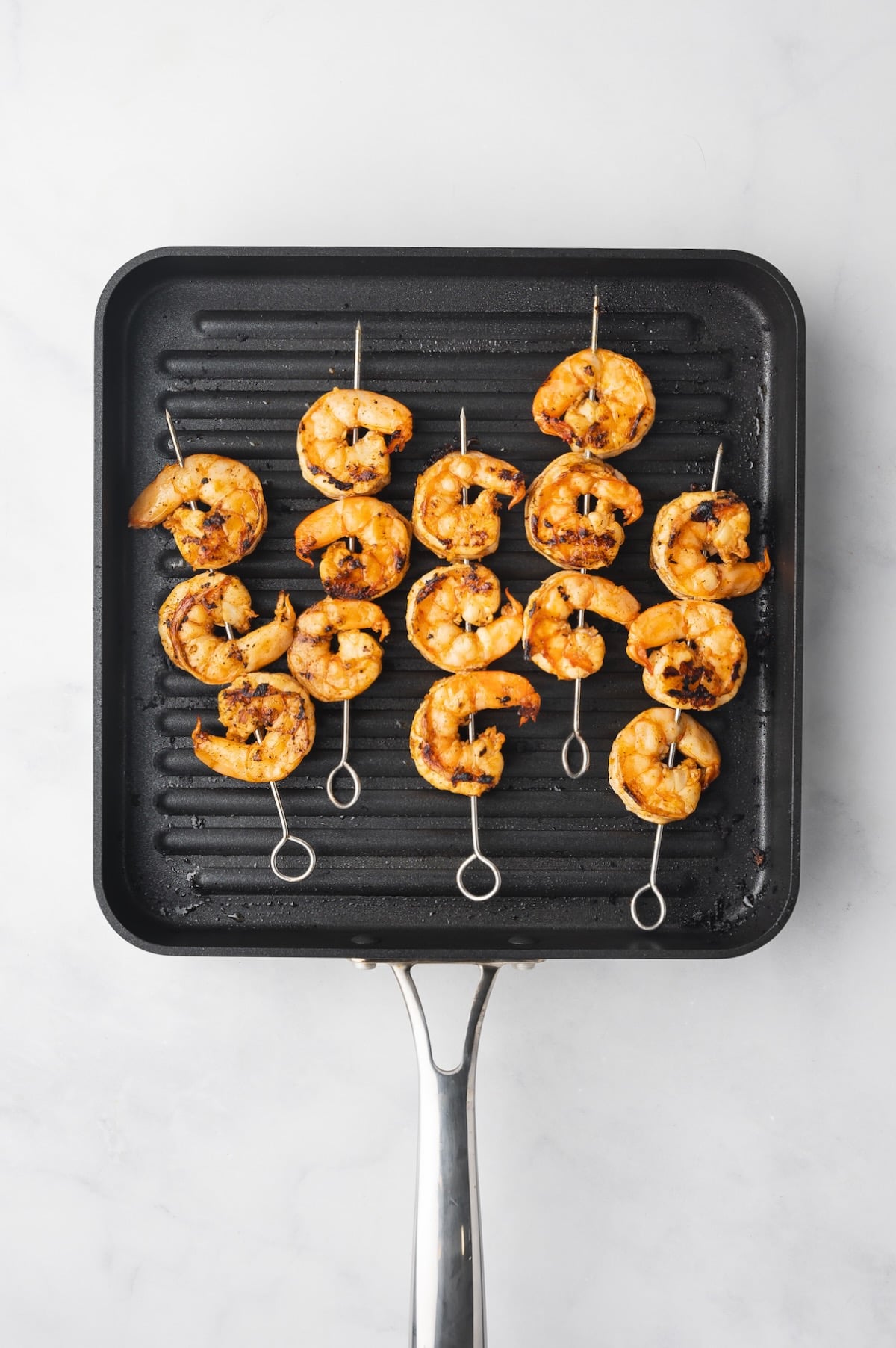 Grilled shrimp skewers on square grill pan.