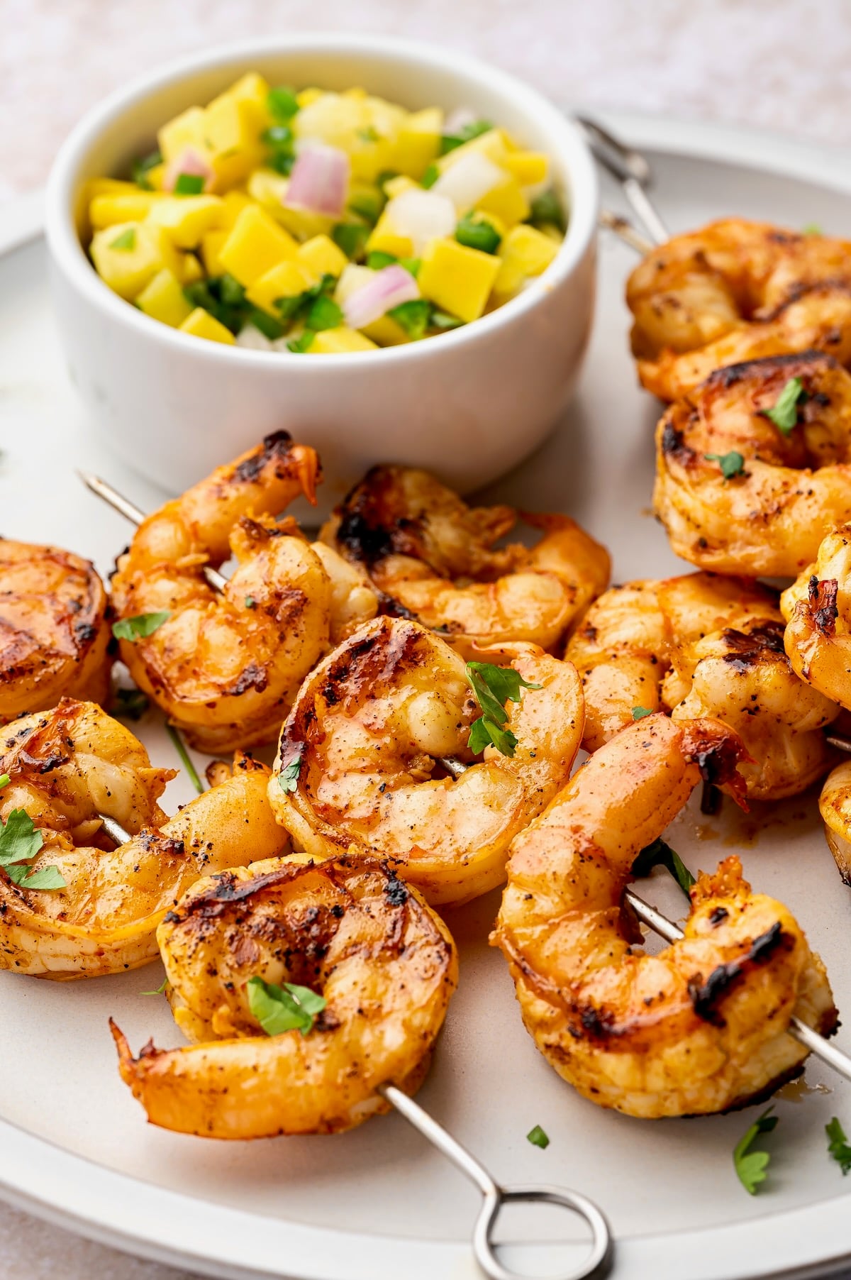 Grilled Shrimp Skewers on white plate with Pineapple Mango Salsa in small white bowl.