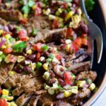 Grilled Skirt Steak with Black Bean Tomato Corn Salad on black platter with serving fork.