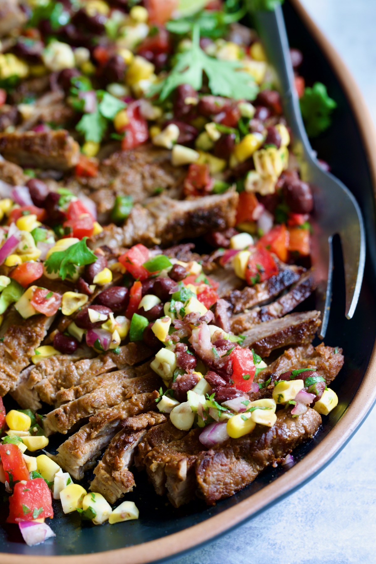 Grilled Skirt Steak with Black Bean Tomato Corn Salad on black platter with serving fork.