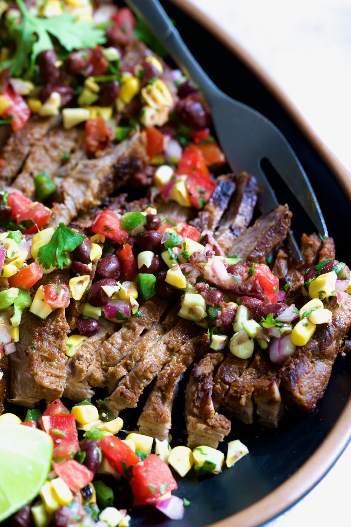 Grilled Skirt Steak with Black Bean Corn Tomato Salad on black platter.