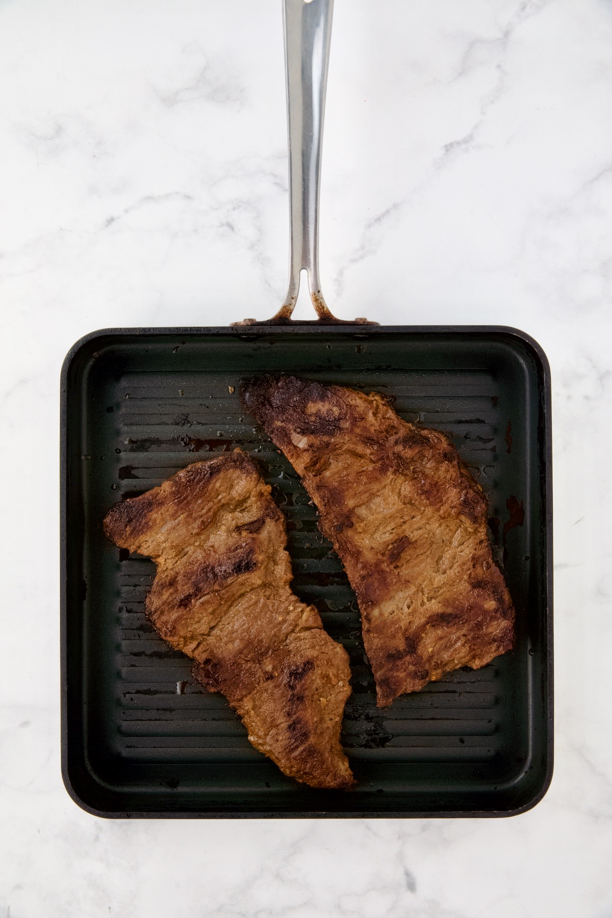 Two pieces of grilled skirt steak on grill pan.
