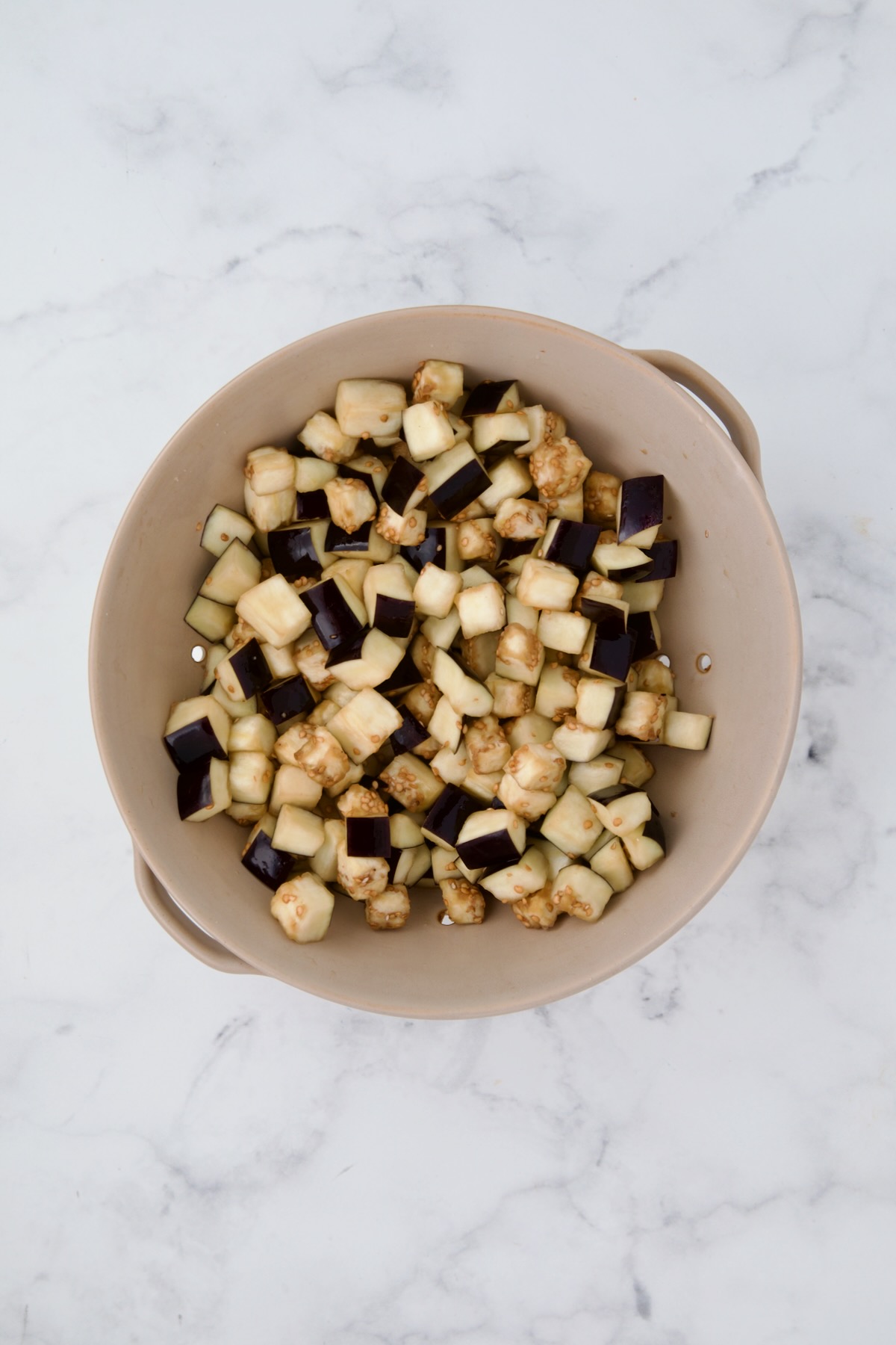 Cubes of eggplant in beige colander after being salted and drained.
