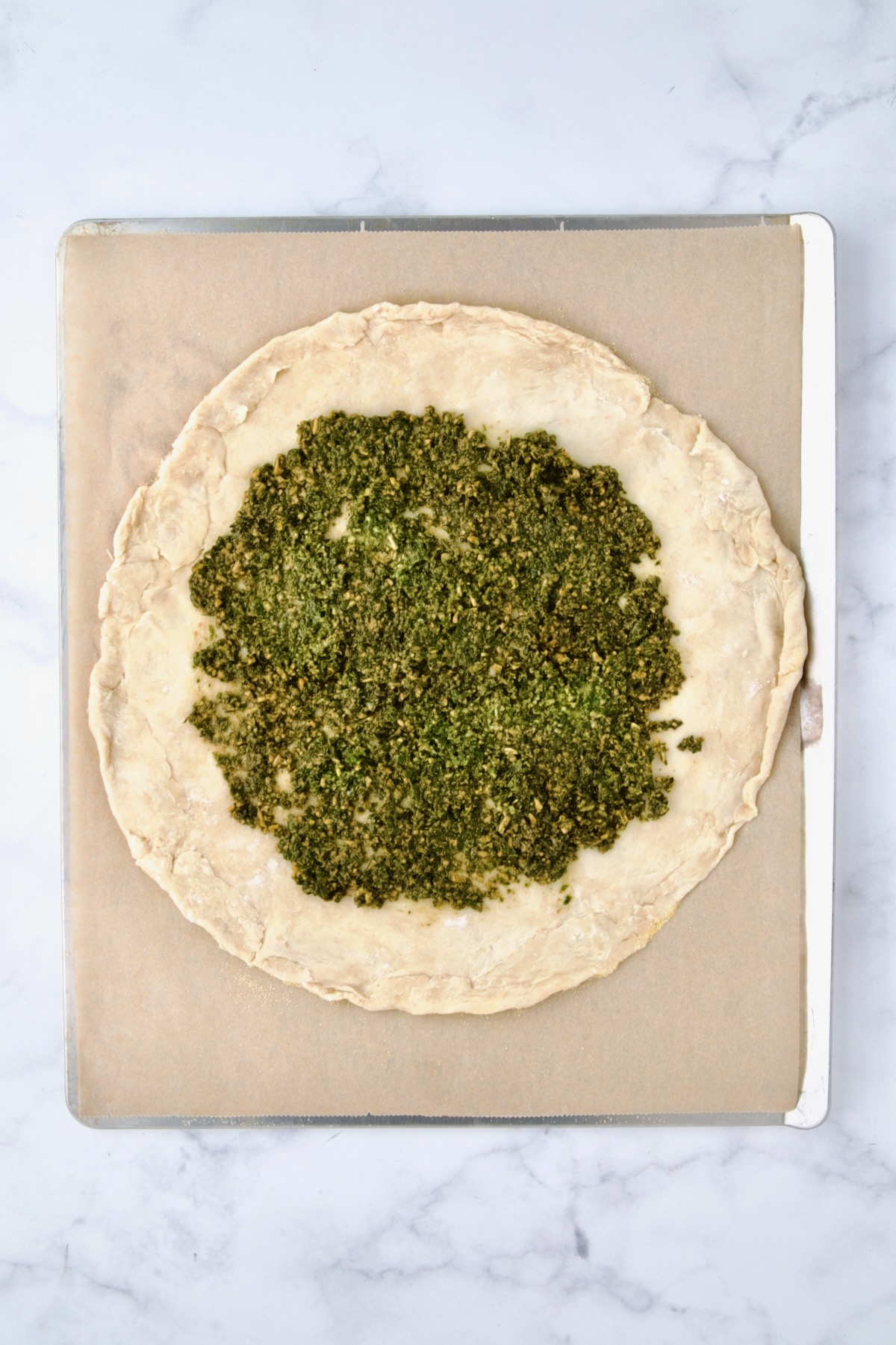 Rolled out galette dough on parchment paper on cookie sheet with pesto added.