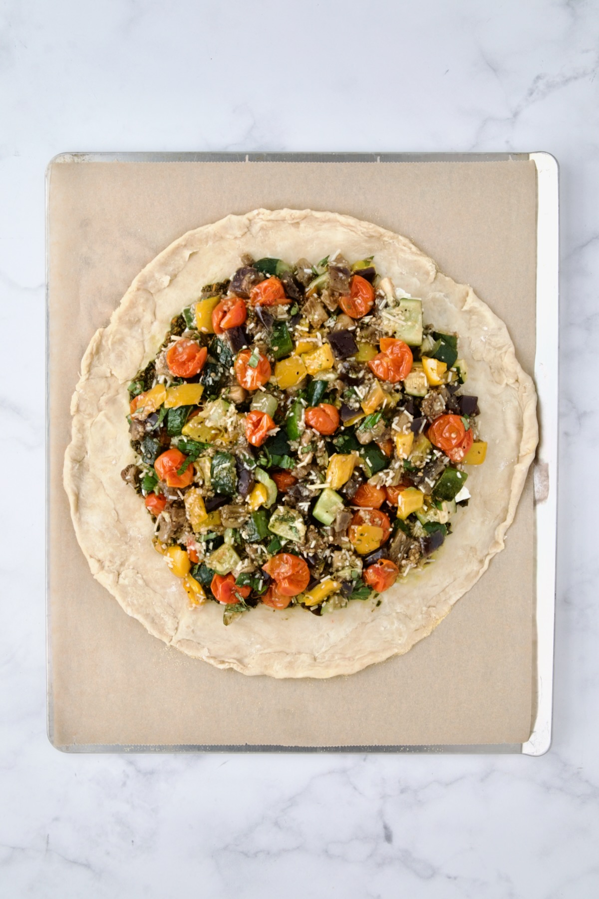 Roasted vegetables added to pesto and goat cheese on rolled out galette dough on parchment paper lined cookie sheet.