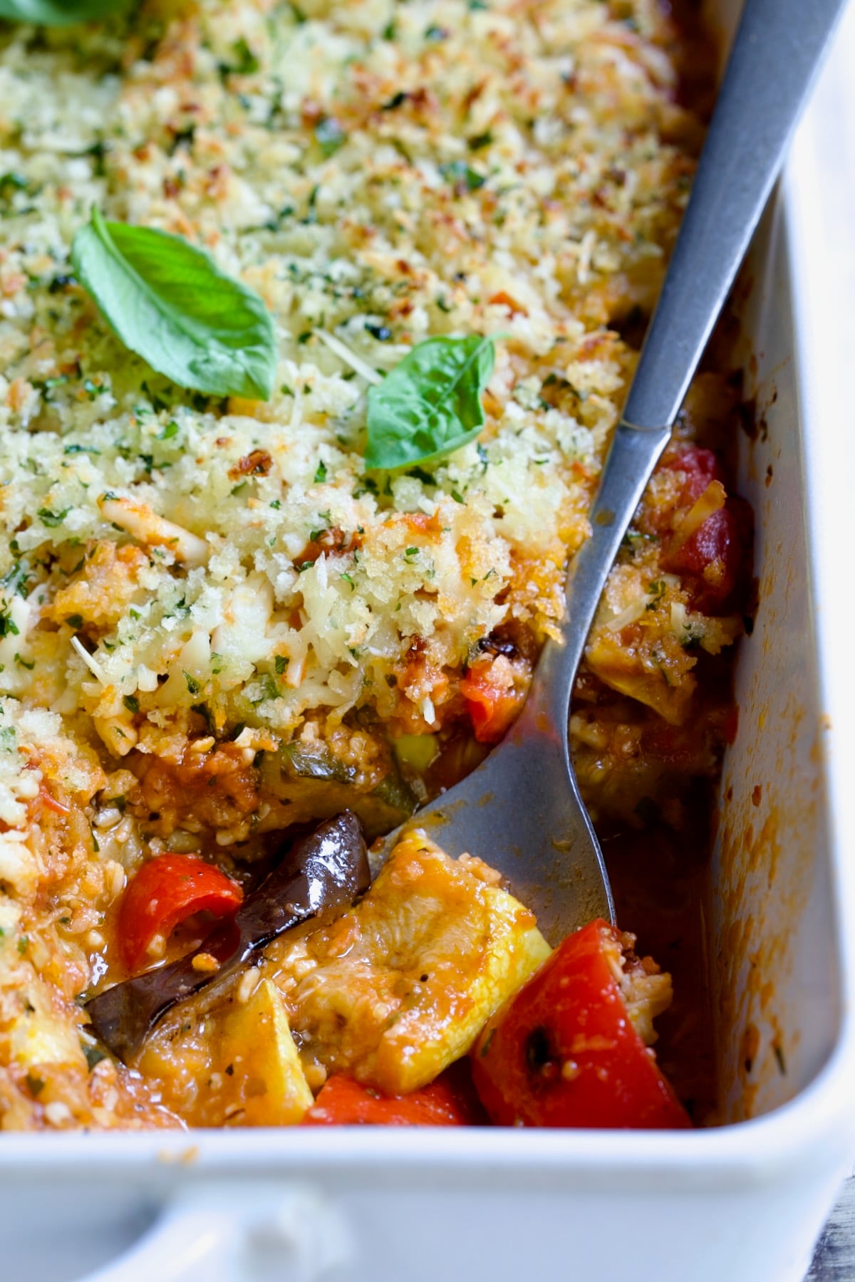Summer Vegetable Parmigiana in white baking dish with serving spoon scooping some up.