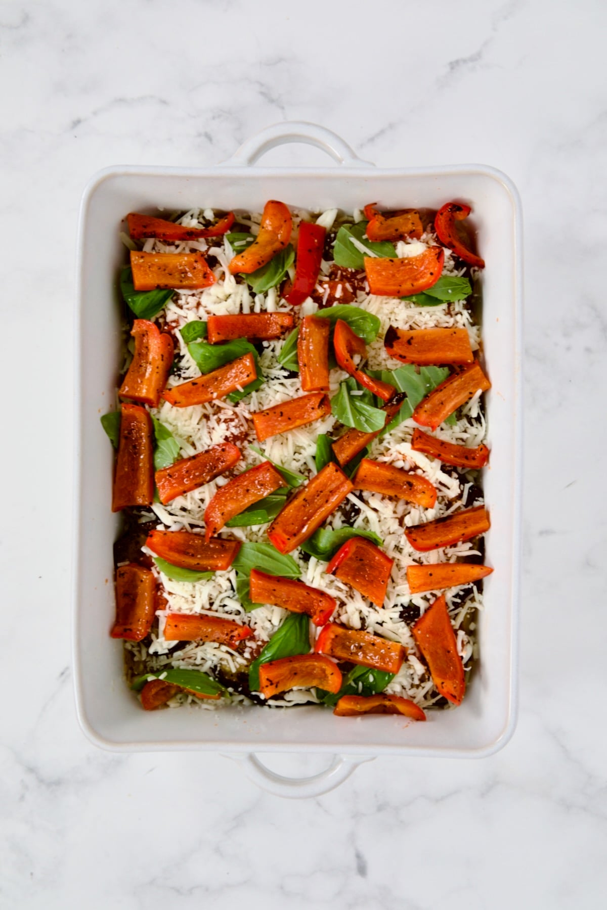 Layer of red bell pepper in white rectangular baking dish.