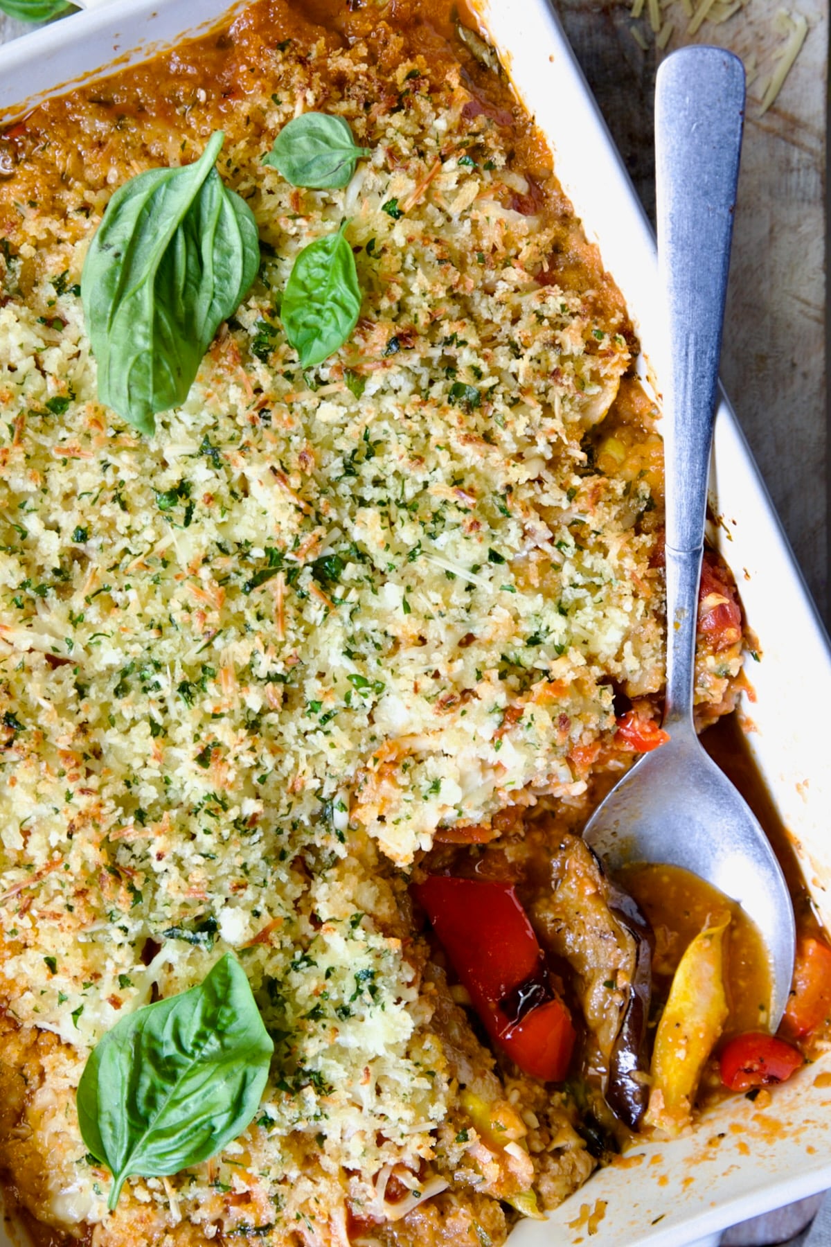 Summer Vegetable Parmigiana in white baking dish with serving spoon scooping some up.