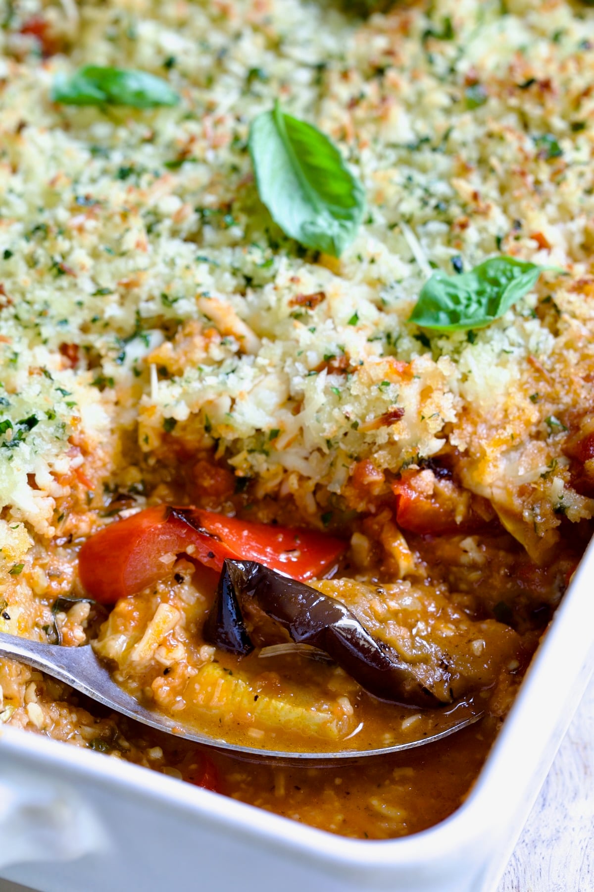 Summer Vegetable Parmigiana in white baking dish with serving spoon scooping some up.