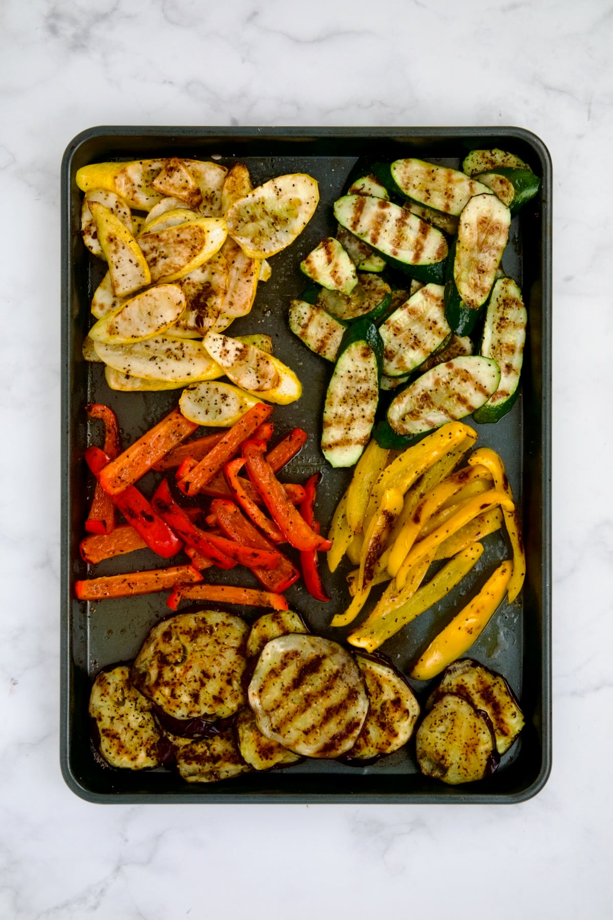 Grilled yellow squash, zucchini, red bell pepper, yellow bell pepper and eggplant on rimmed sheet pan.