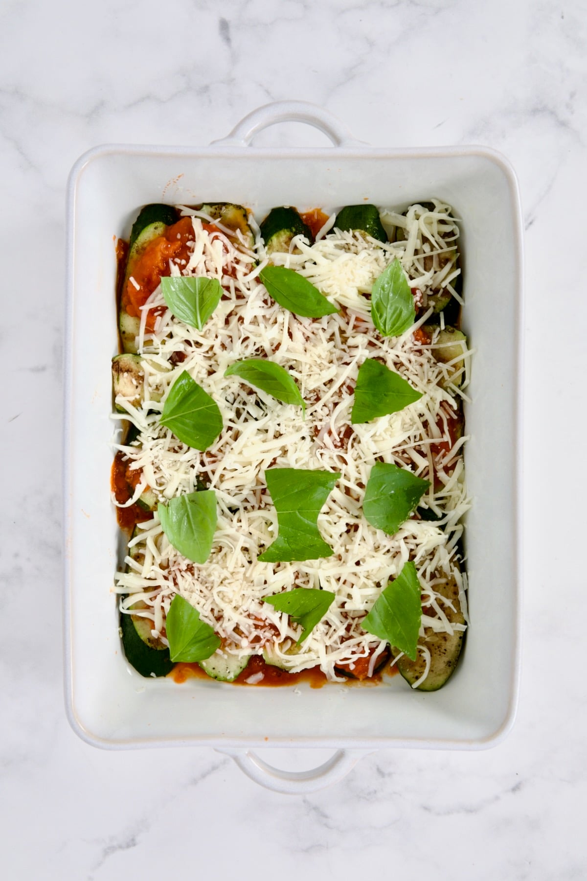 Layer of sauce, cheese and basil in white rectangular baking dish.