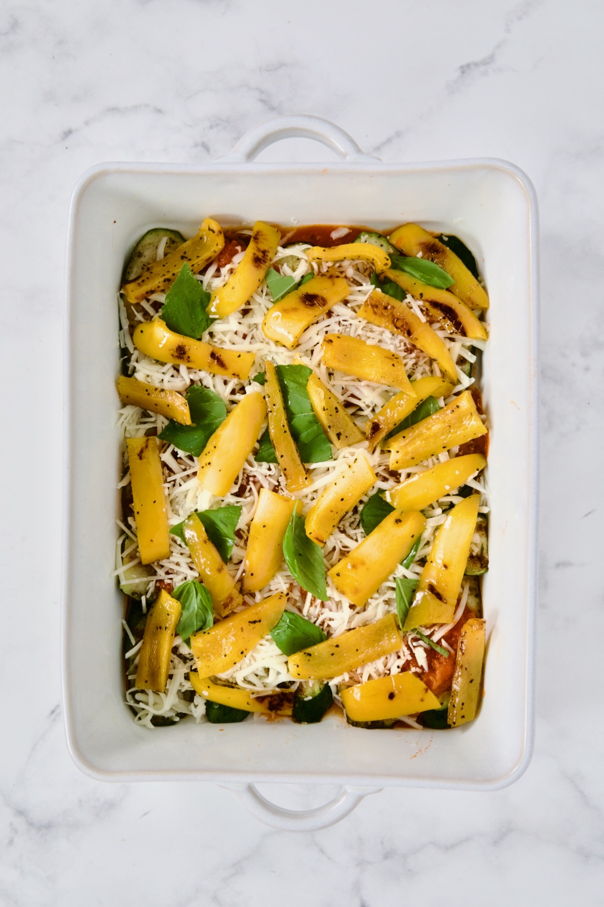 Layer of yellow bell pepper in white rectangular baking dish.