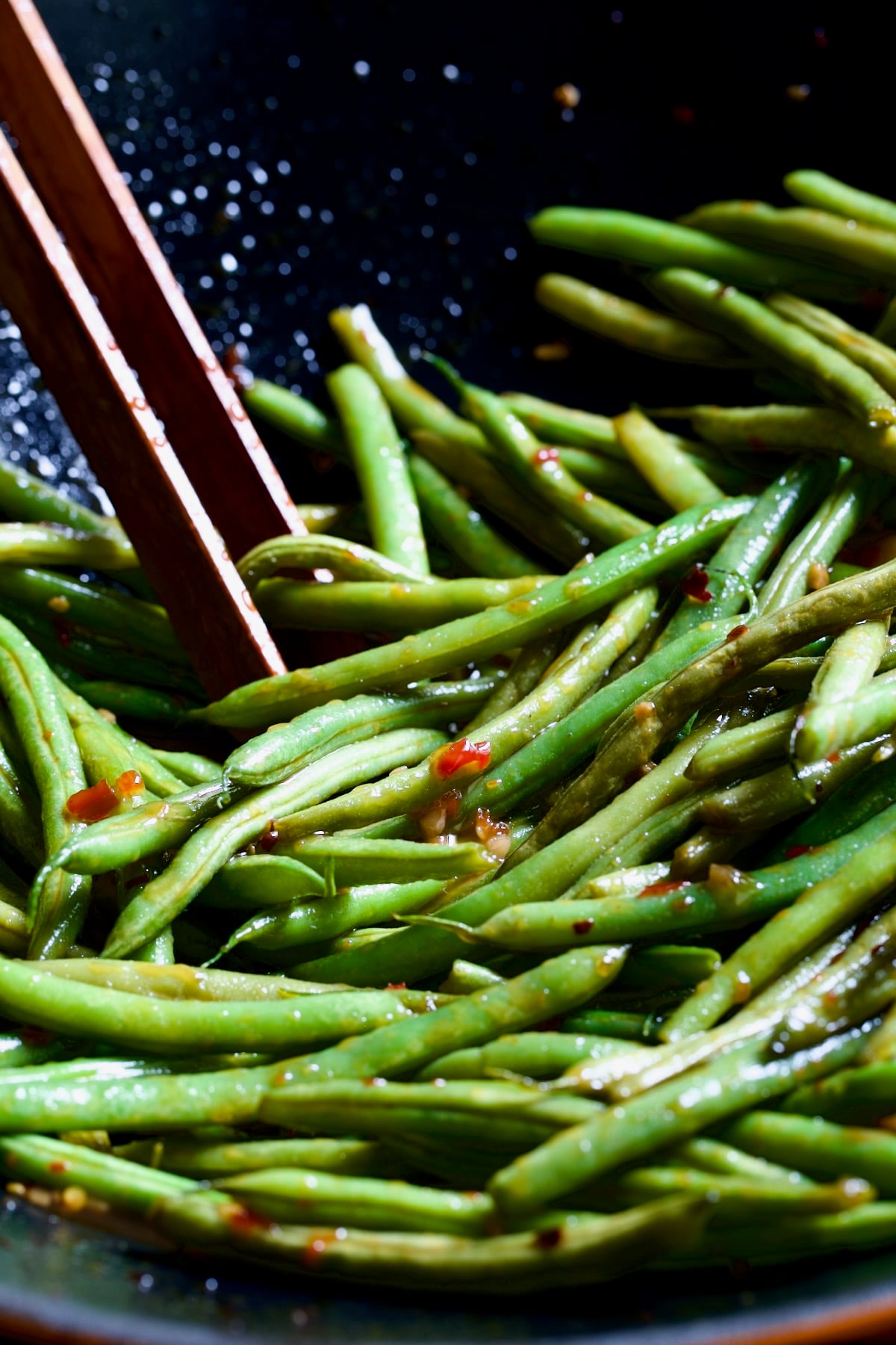 Thai Sweet Chili Green Beans in wok being stirred with wooden tongs.