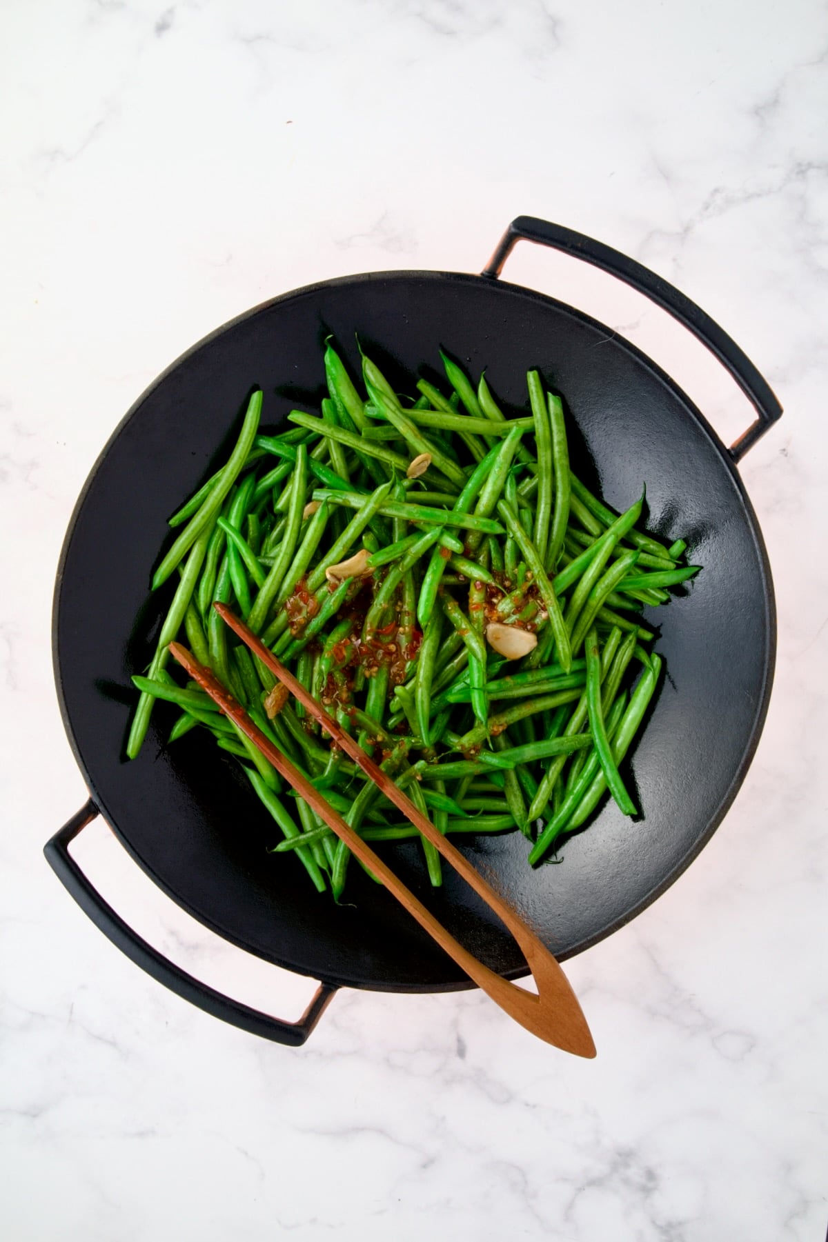 Green Beans and sliced garlic in black iron wok with sauce added.