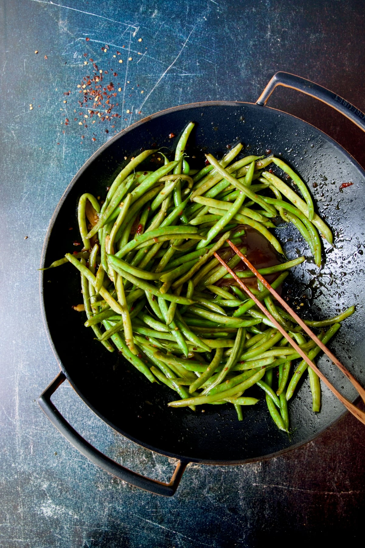 Thai Sweet Chili Green Beans in wok pushed to one side being stirred with wooden tongs.