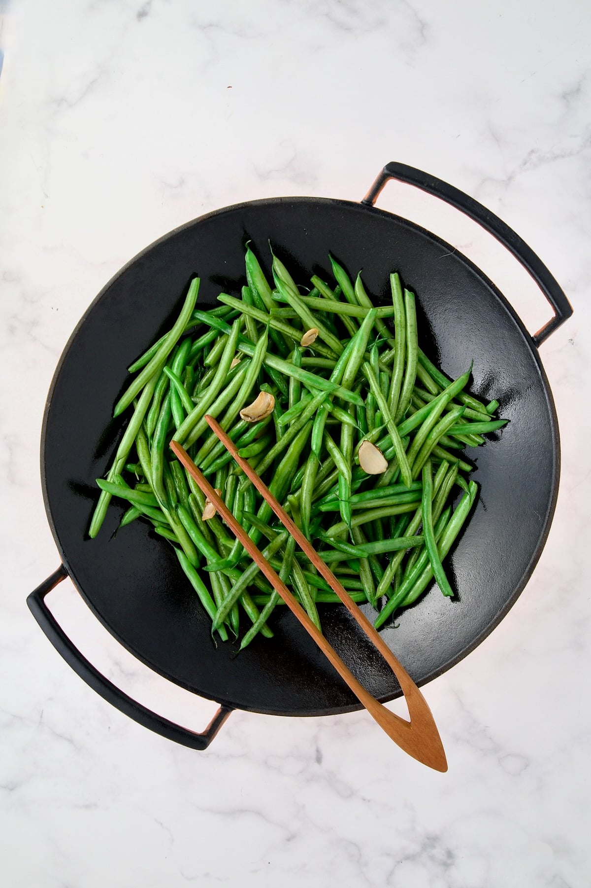 Green Beans and sliced garlic in black iron wok.