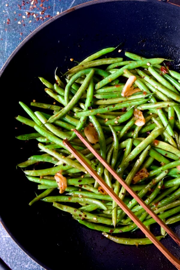 Thai Sweet Chili Green Beans in wok being stirred with wooden tongs.