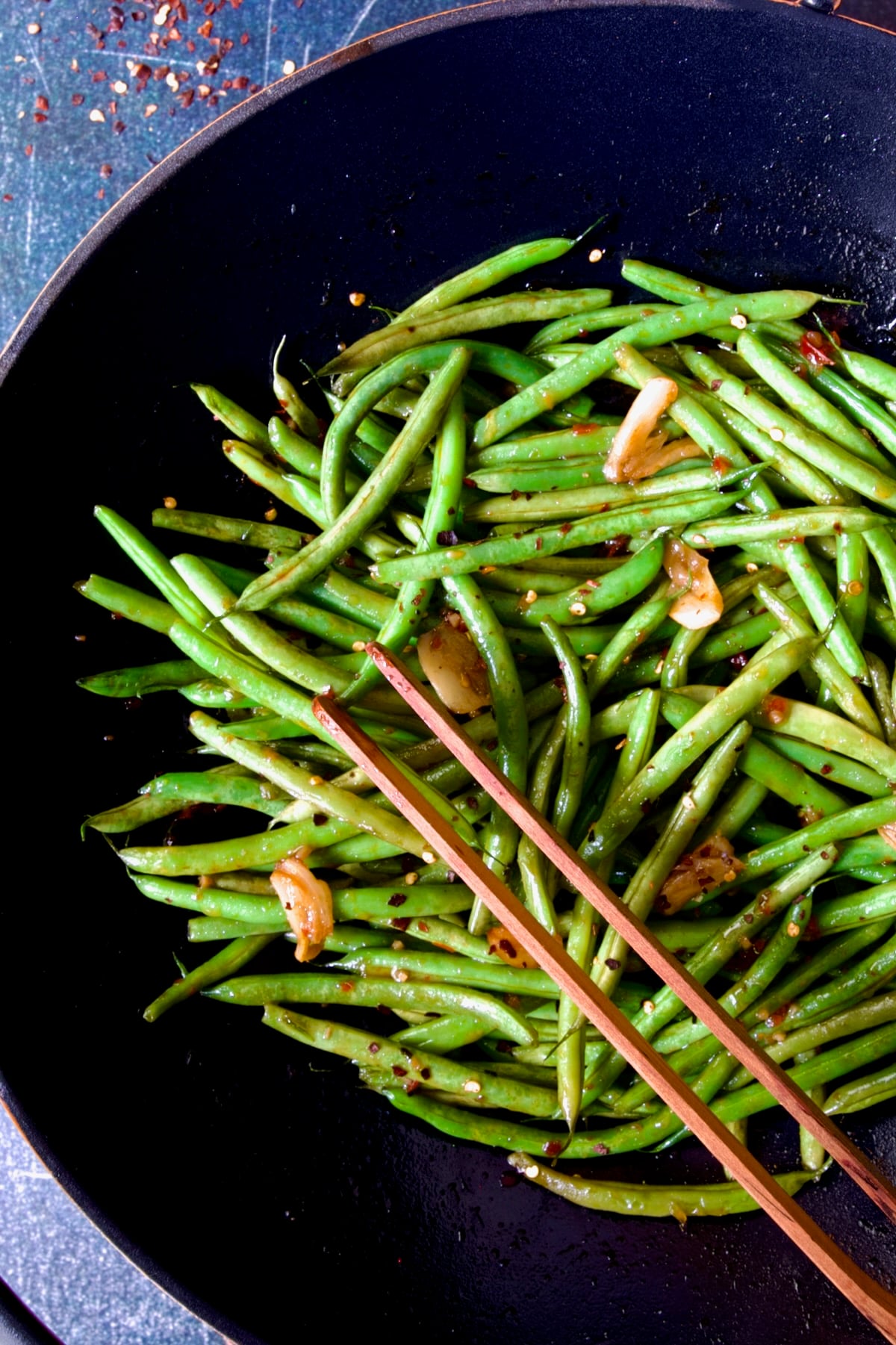 Thai Sweet Chili Green Beans in wok being stirred with wooden tongs.