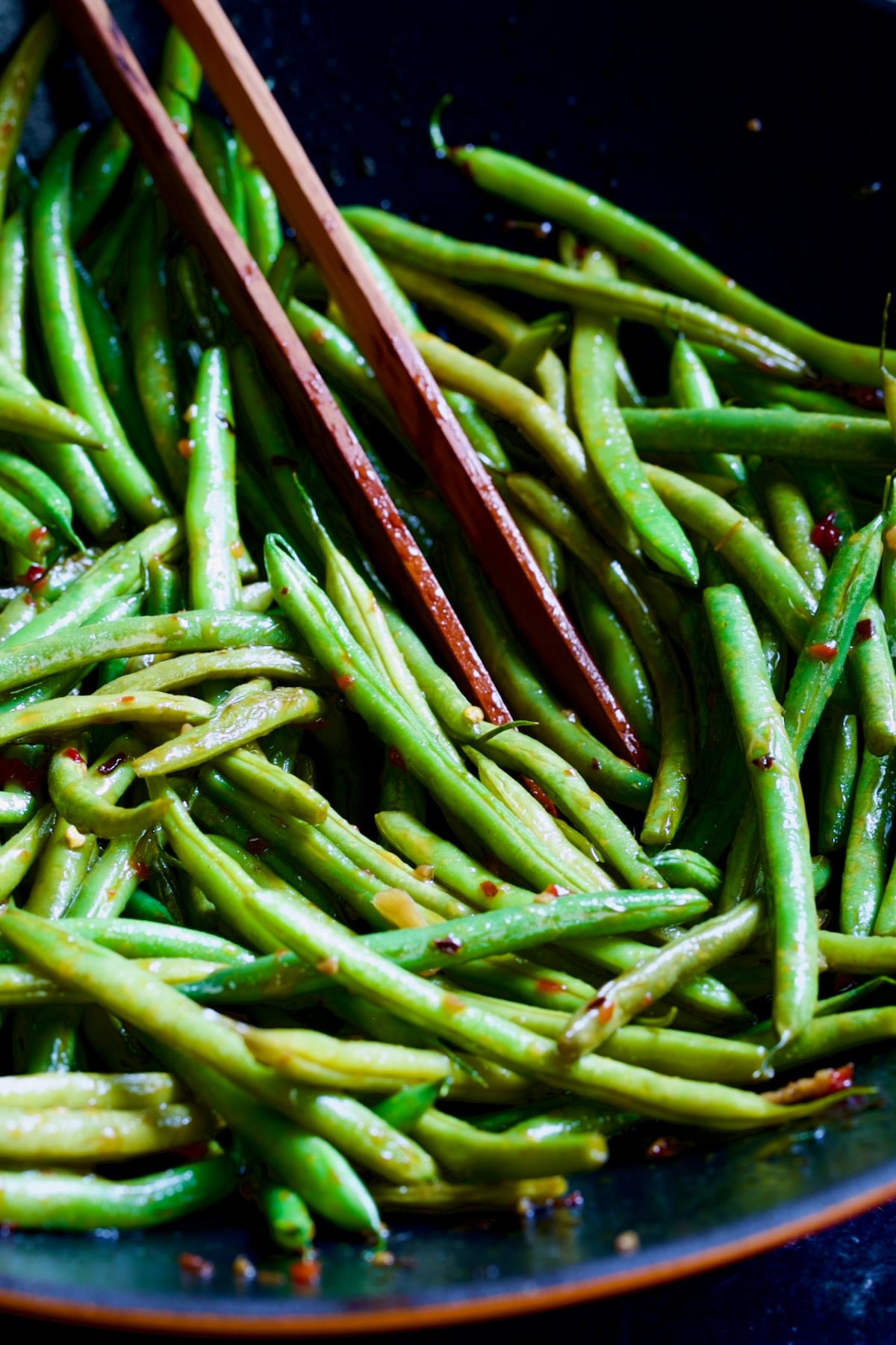 Thai Sweet Chili Green Beans in wok being stirred with wooden tongs.