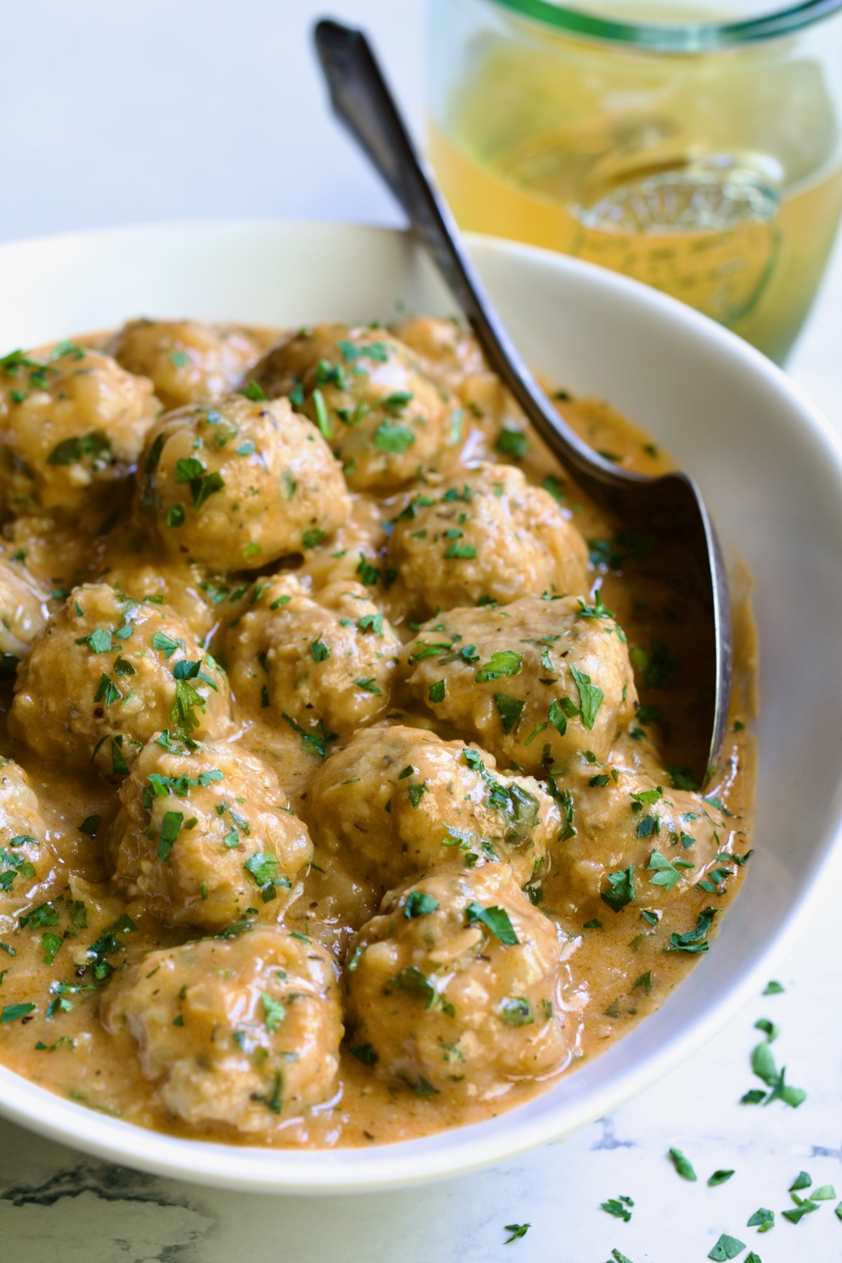 Baked Turkey Meatballs in Beer - Onion Sauce in white oval bowl with serving spoon garnished with fresh parsley.