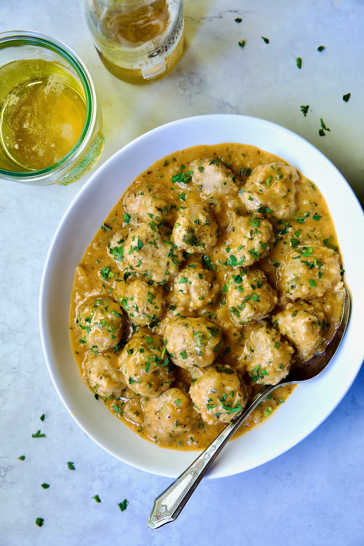 Baked Turkey Meatballs in Beer - Onion Sauce in white oval bowl with serving spoon garnished with fresh parsley.