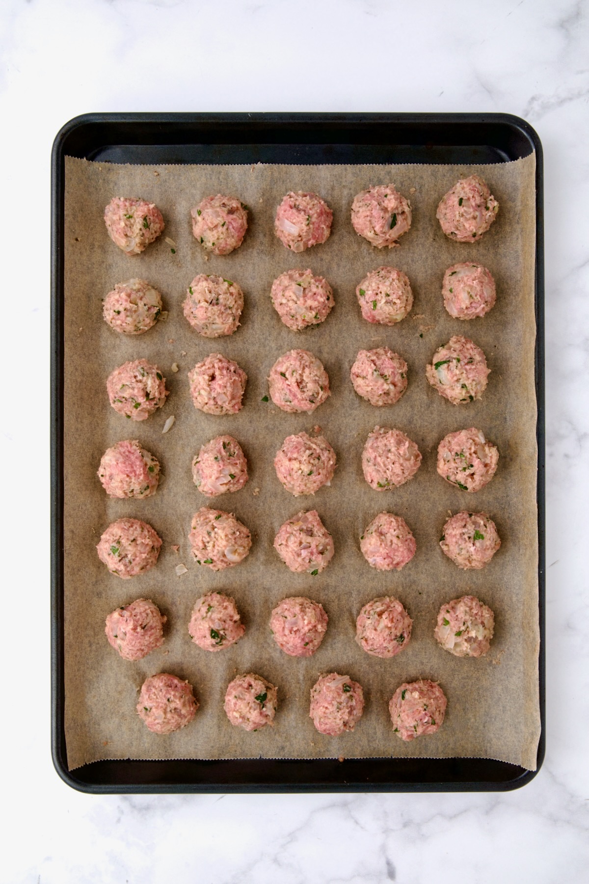 34 turkey meatballs on parchment paper on rimmed sheet pan before being baked.