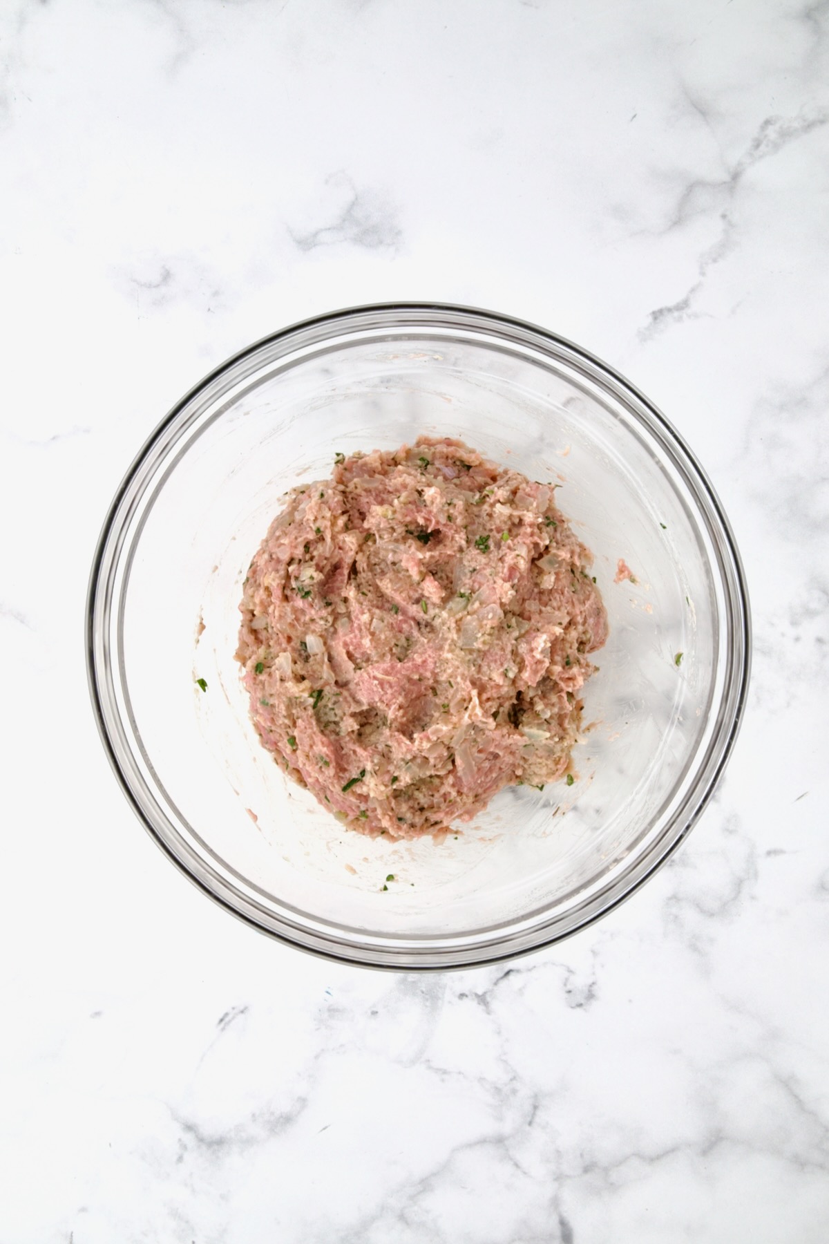 Ingredients for turkey meatballs with ground turkey in glass bowl before being mixed together.