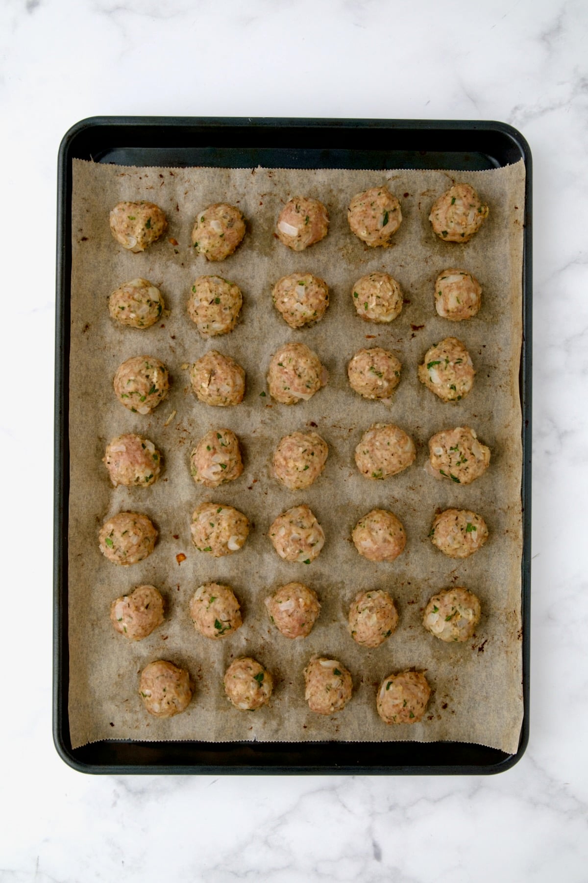 34 turkey meatballs on parchment paper on rimmed sheet pan after being baked.