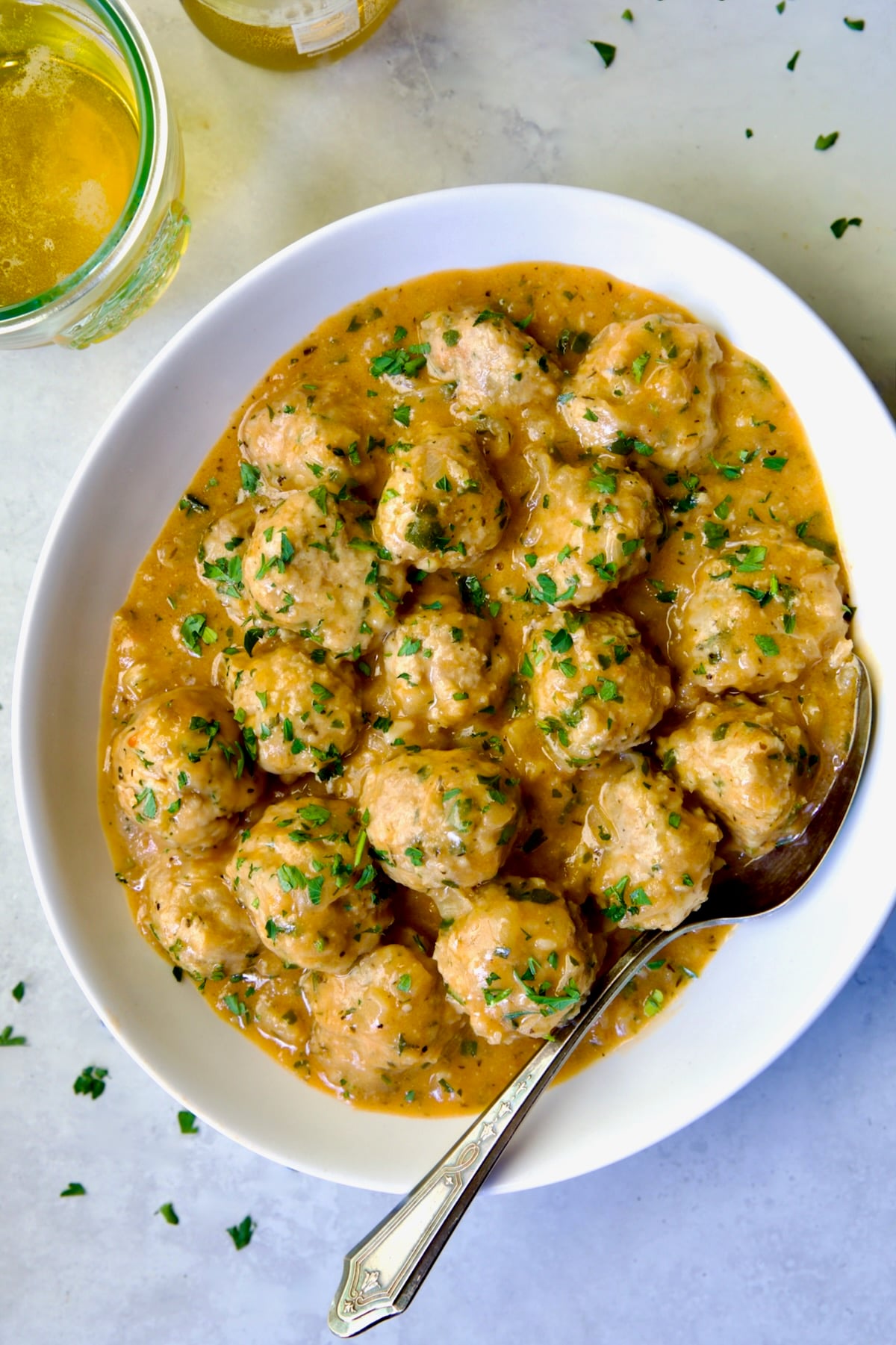 Baked Turkey Meatballs in Beer - Onion Sauce in white oval bowl with serving spoon garnished with fresh parsley.