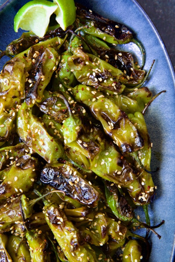 Blistered Shishito Peppers on blue oval platter garnished with sesame seeds.